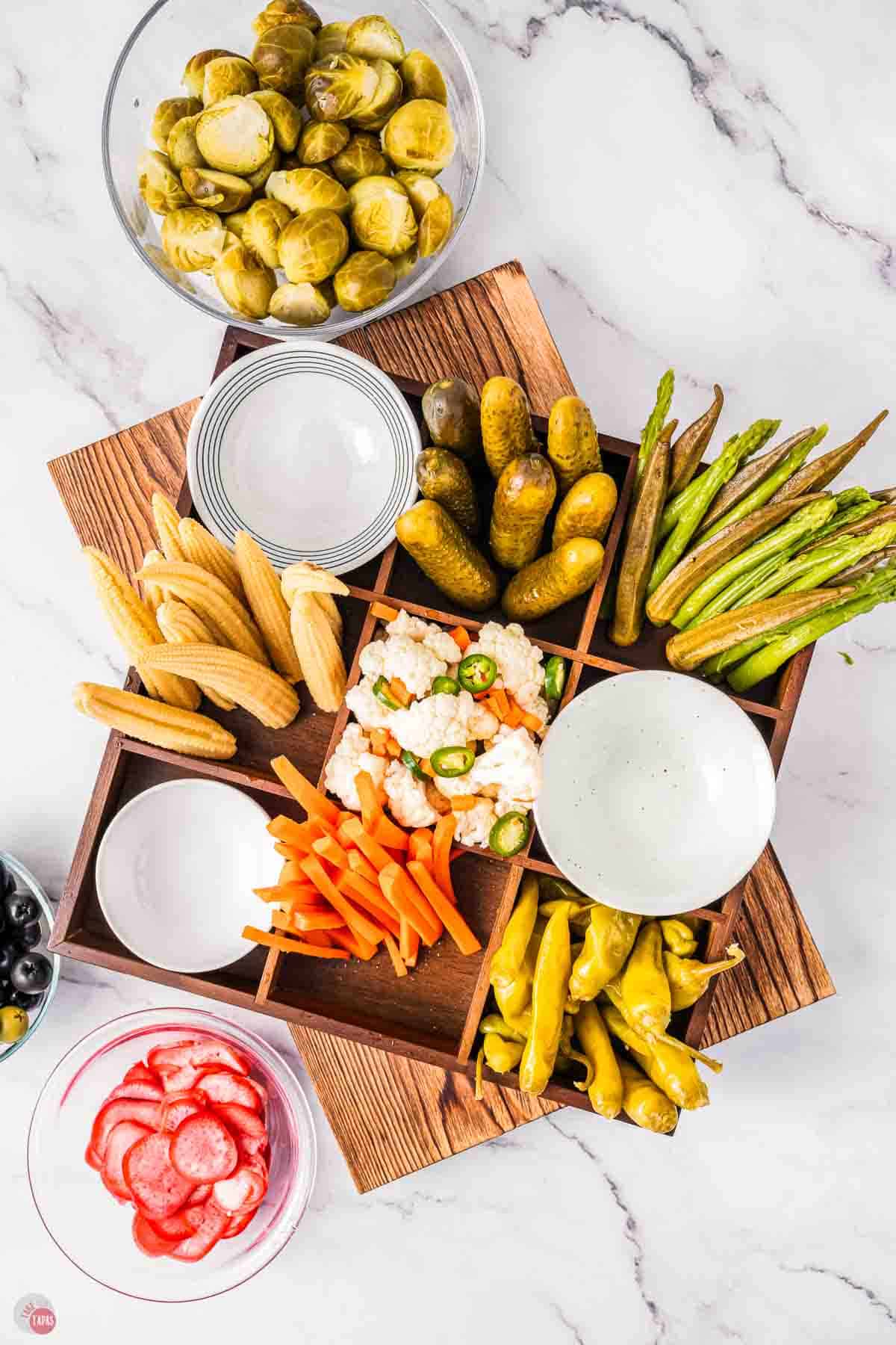 assorted pickles in a 9 square wood tray and white bowls