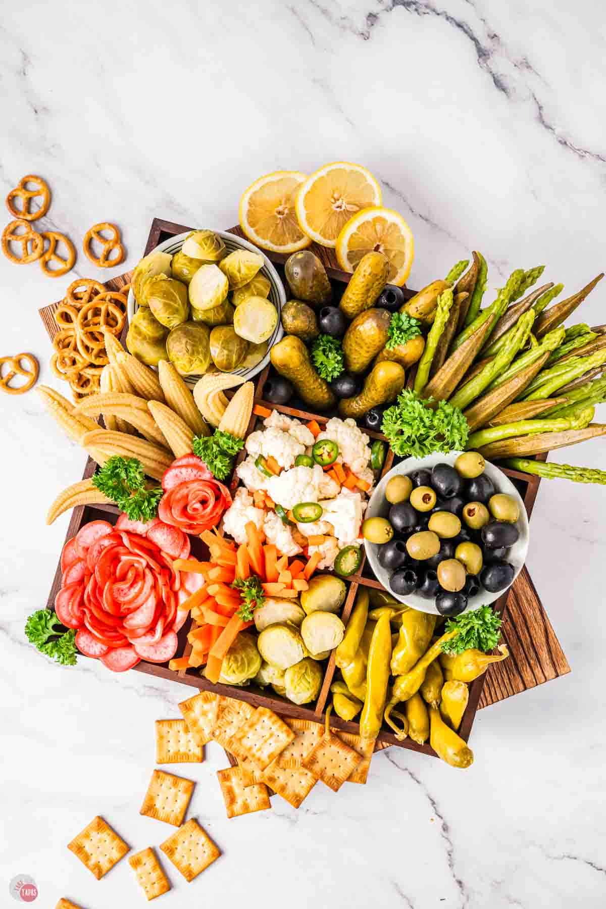 relish tray on wood board with pretzels and crackers around it