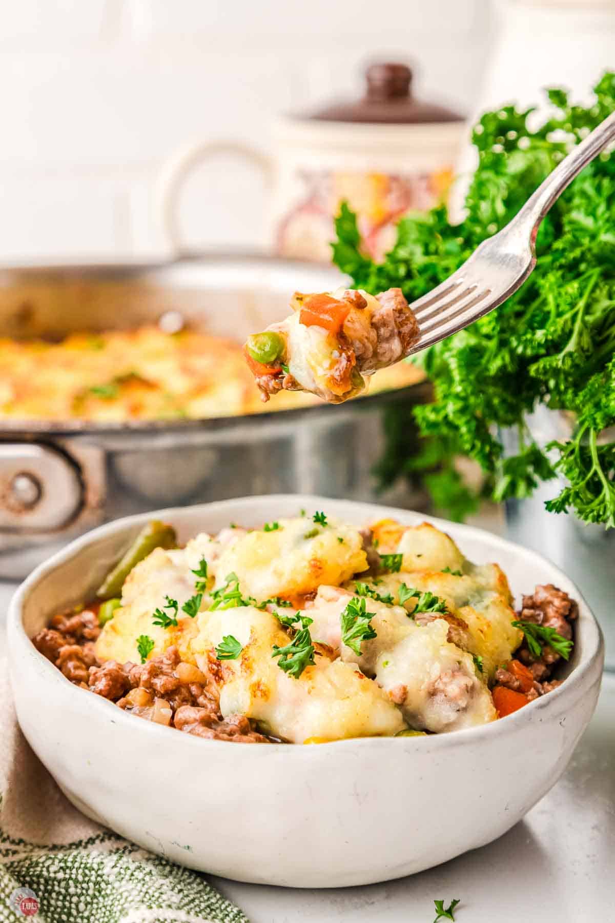 bowl of shepherd's pie with a skillet behind it and a fork