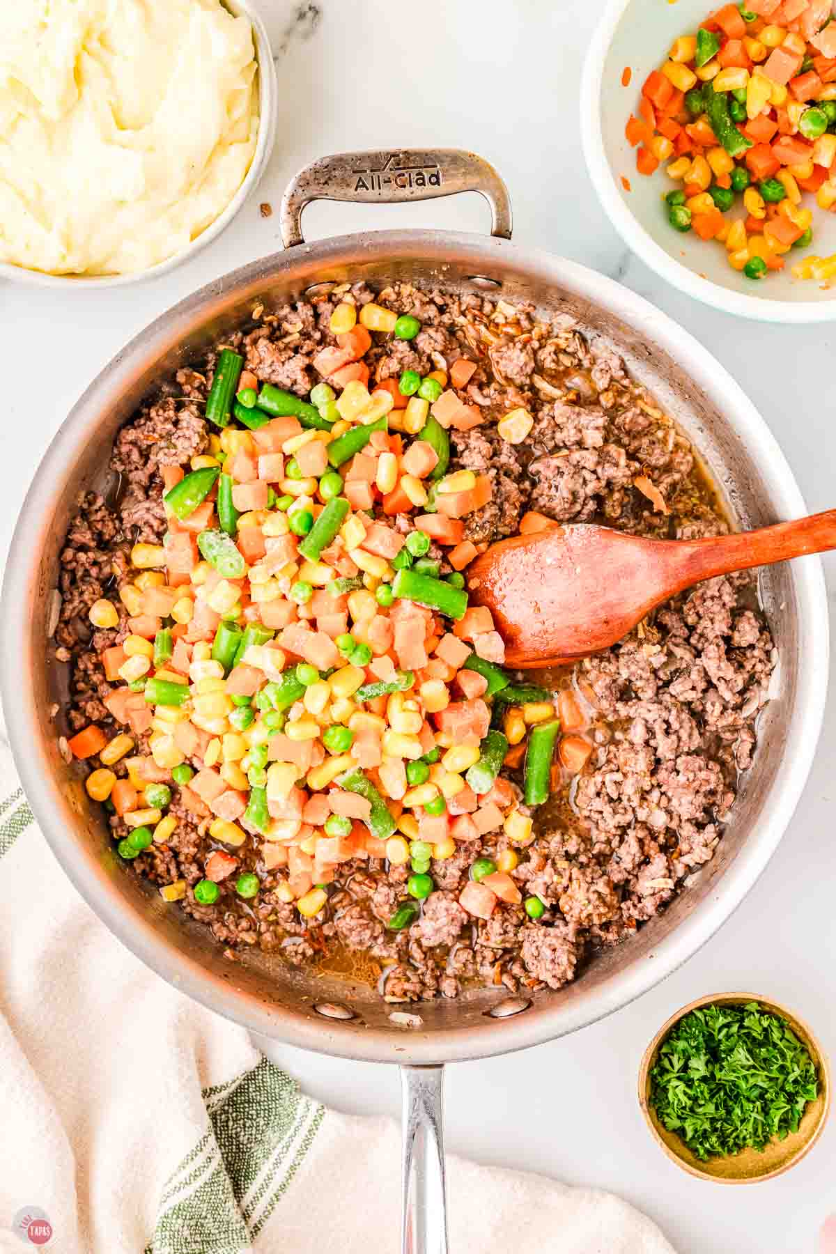 cooked ground beef in a silver skillet with frozen mixed vegetables on top
