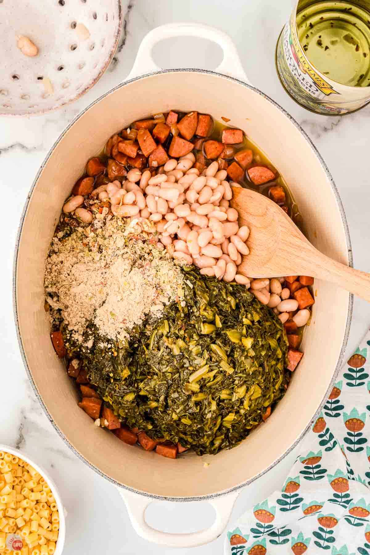 pot with cooked smoked sausage, collar greens, and beans with a wood spoon