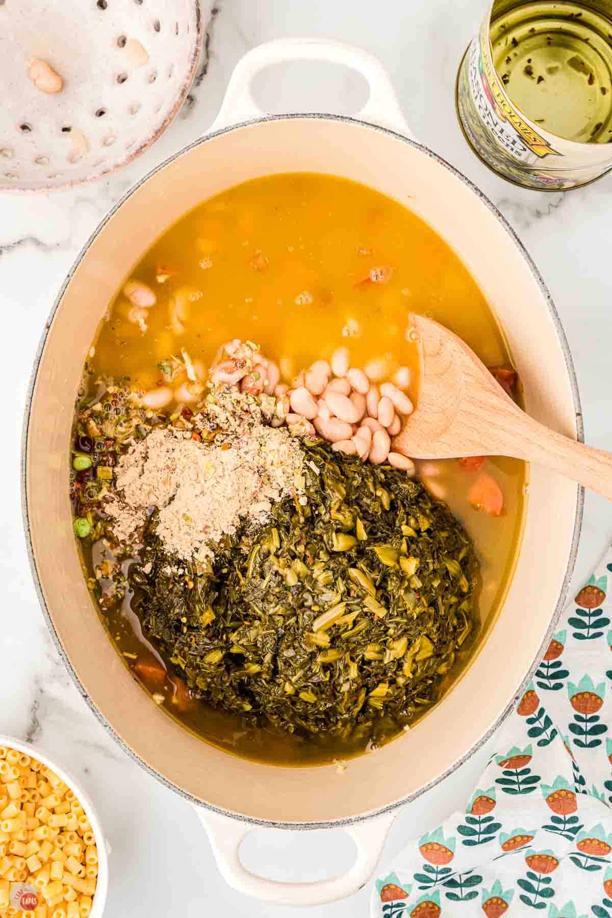 broth and beans being stirred in a pot with  greens