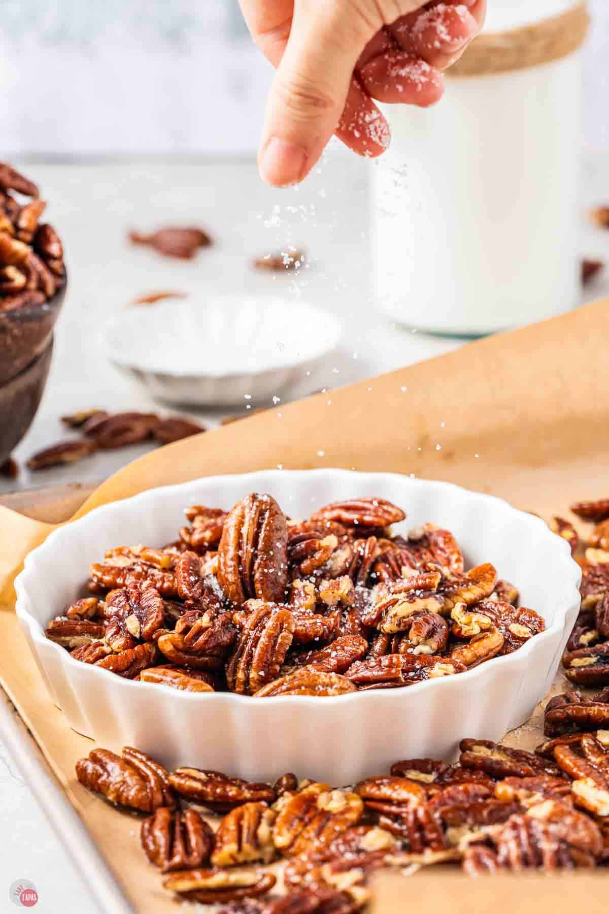hand sprinkling salt over a bowl of pecans