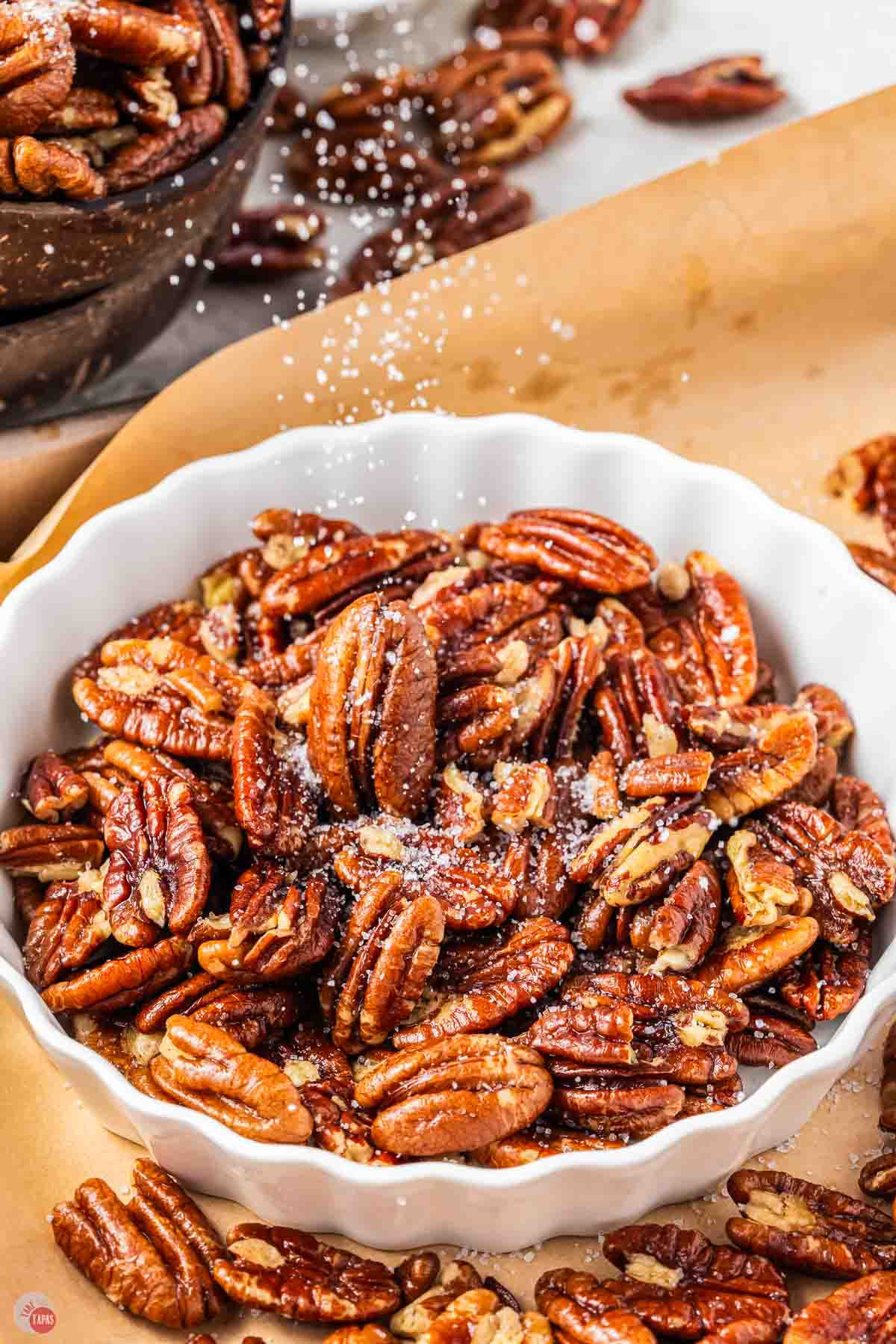 bowl of nuts with salt being sprinkled on them