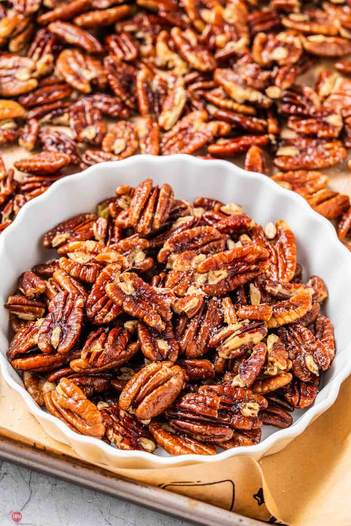 nuts in a white bowl on top of a baking sheet