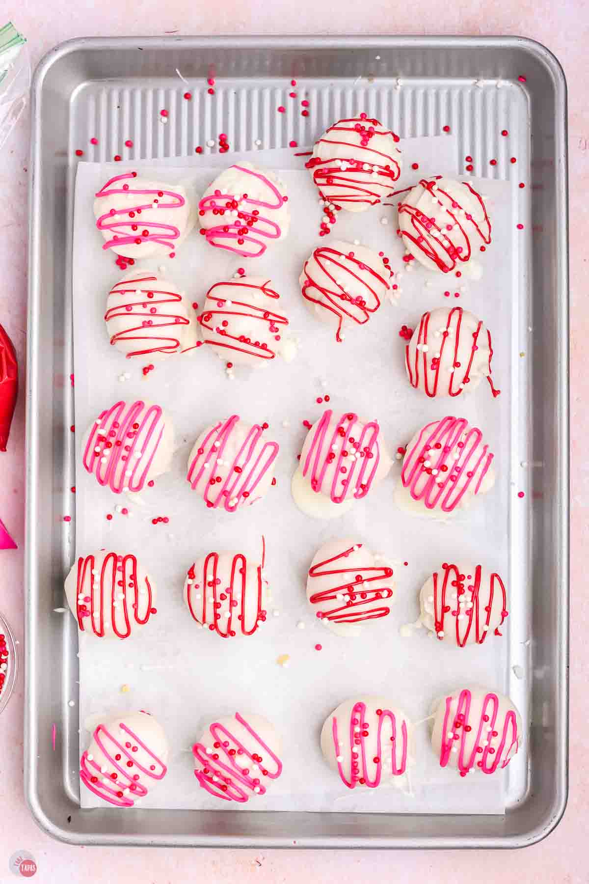 pink and white striped Oreo balls on a parchment lined cookie sheet