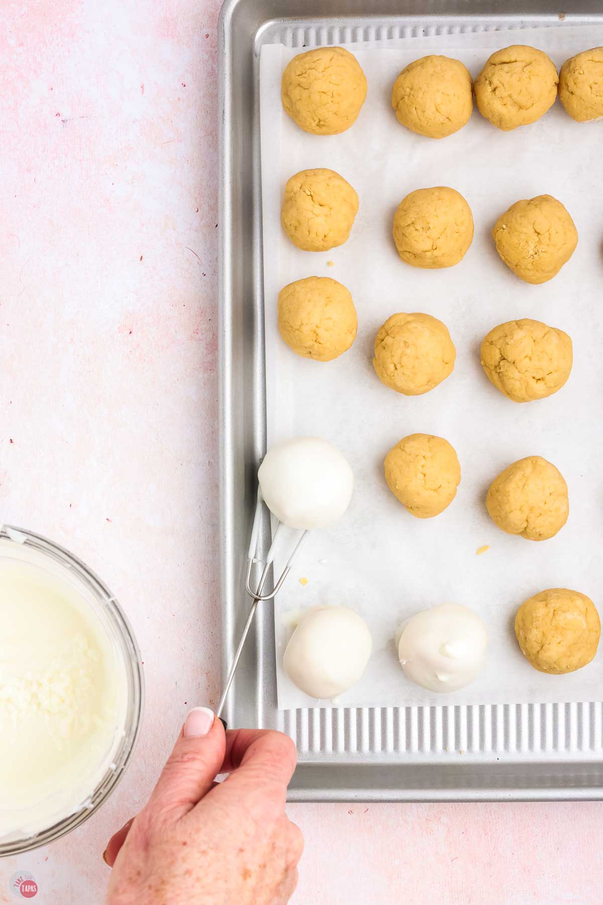baking sheet with balls of cookie dough on it with some being dipped in white chocolate