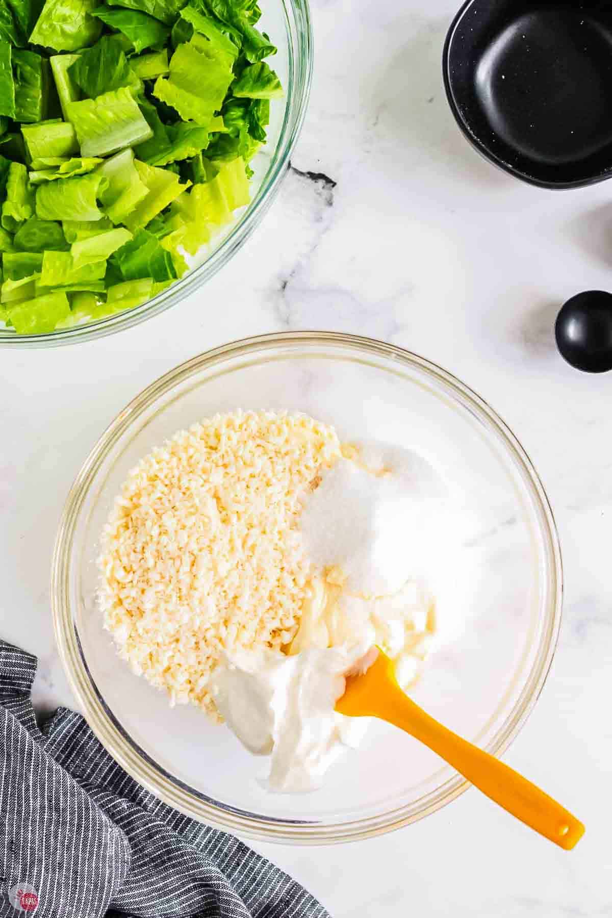 cheese, mayo, and sour cream in a clear bowl with yellow spatula