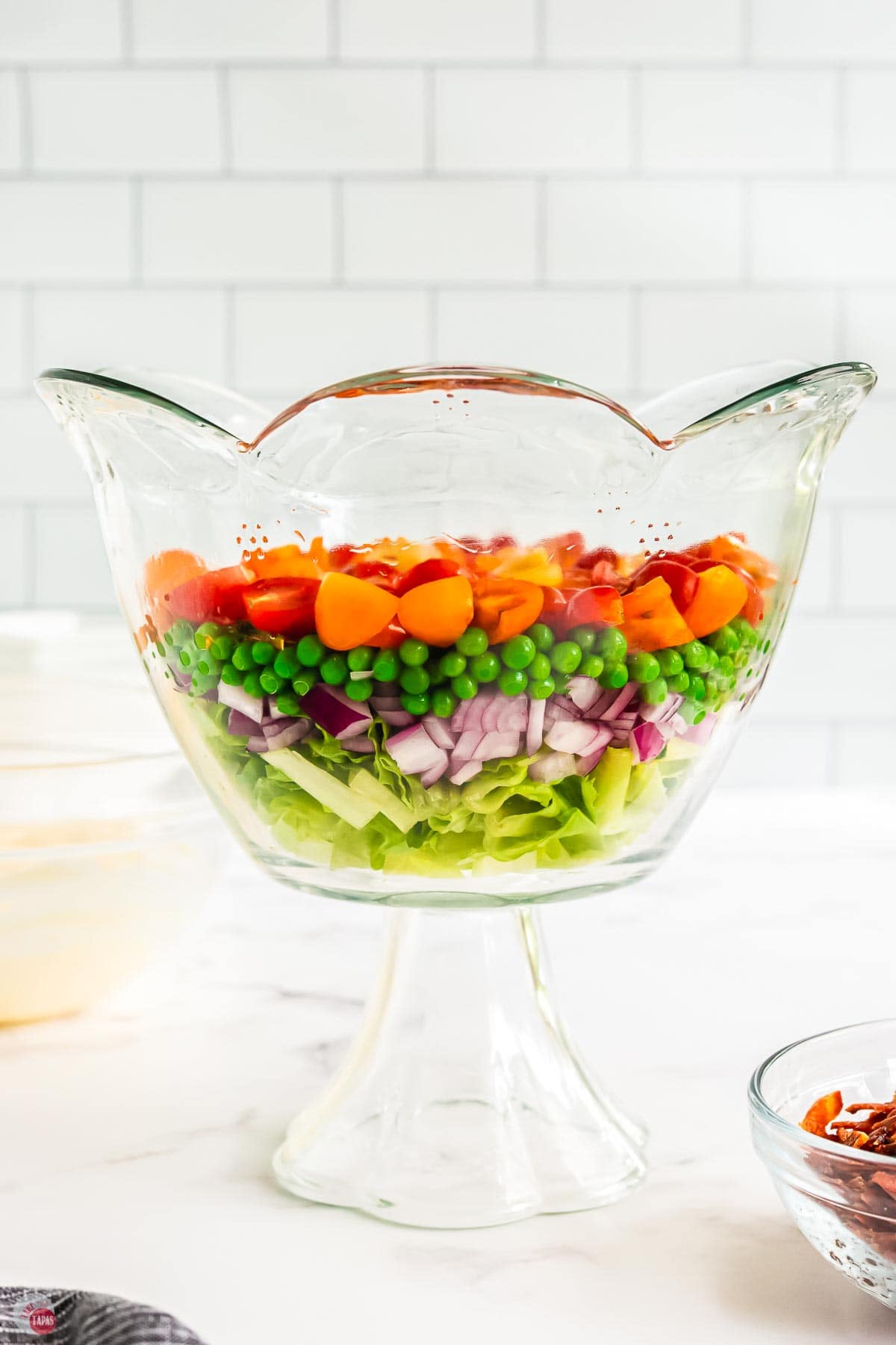 clear trifle bowl with layers of lettuce, peas, onion, and tomatoes