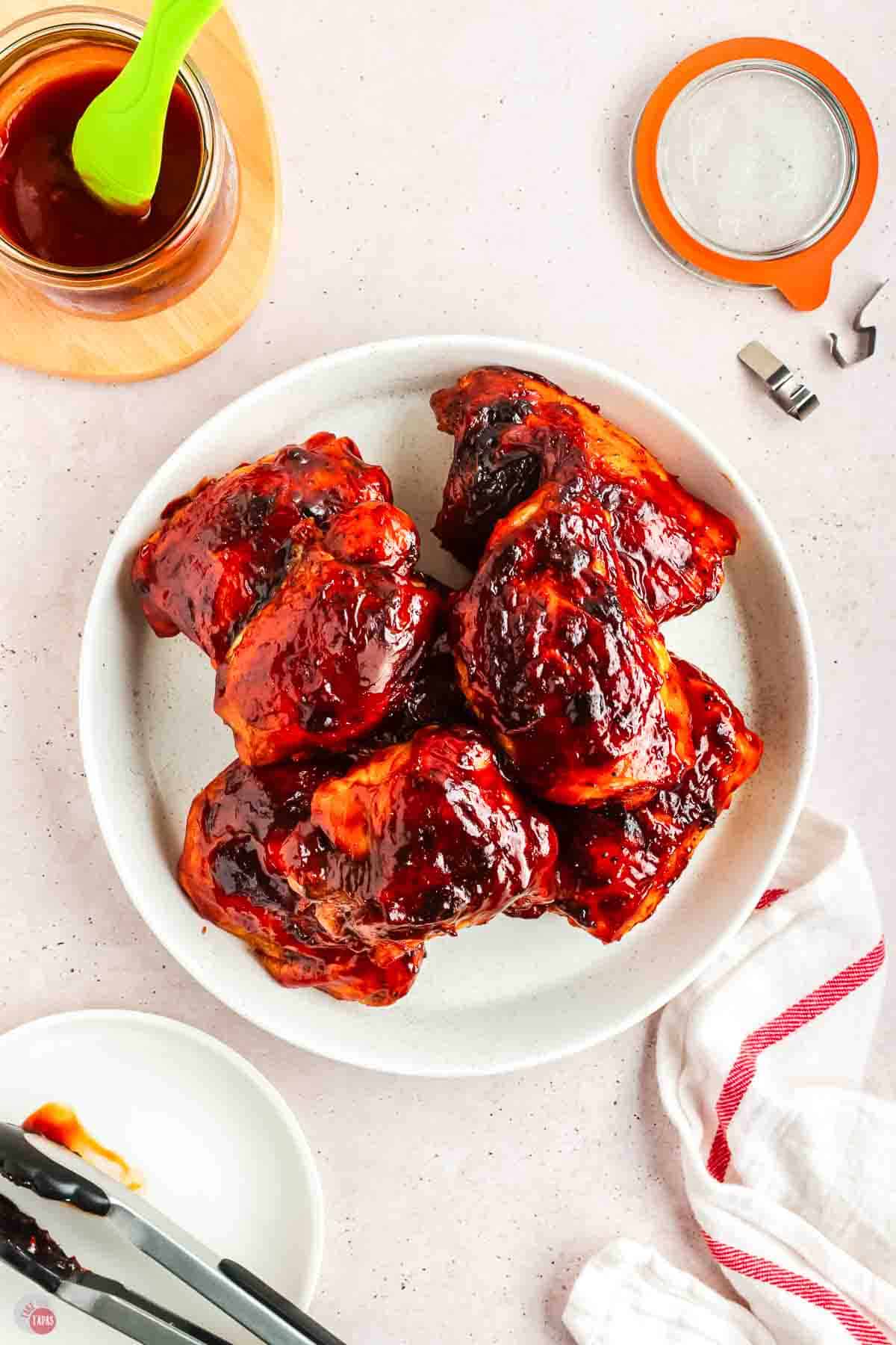 bbq chicken thighs on a white plate next to a striped napkin