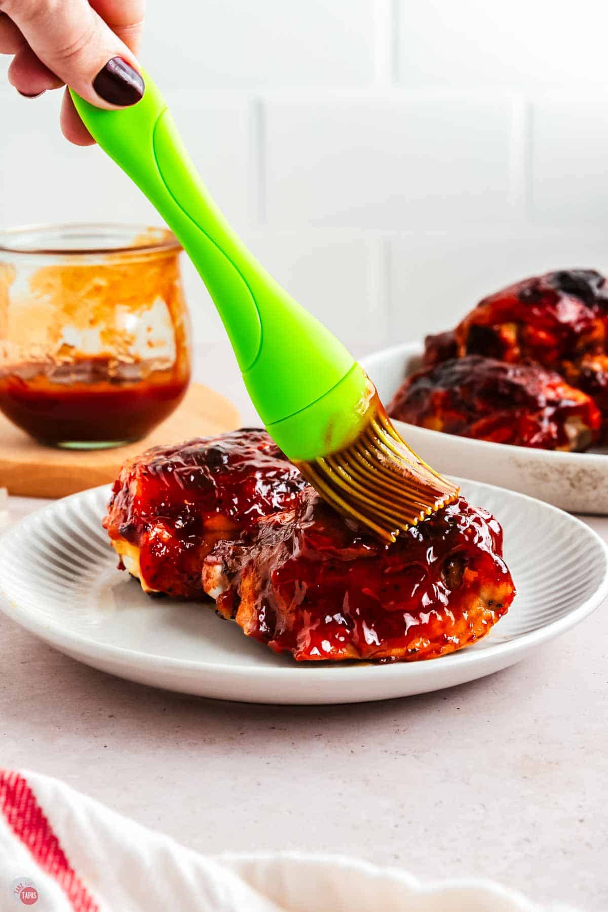 green basting brush applying sauce to a piece of chicken on a white plate