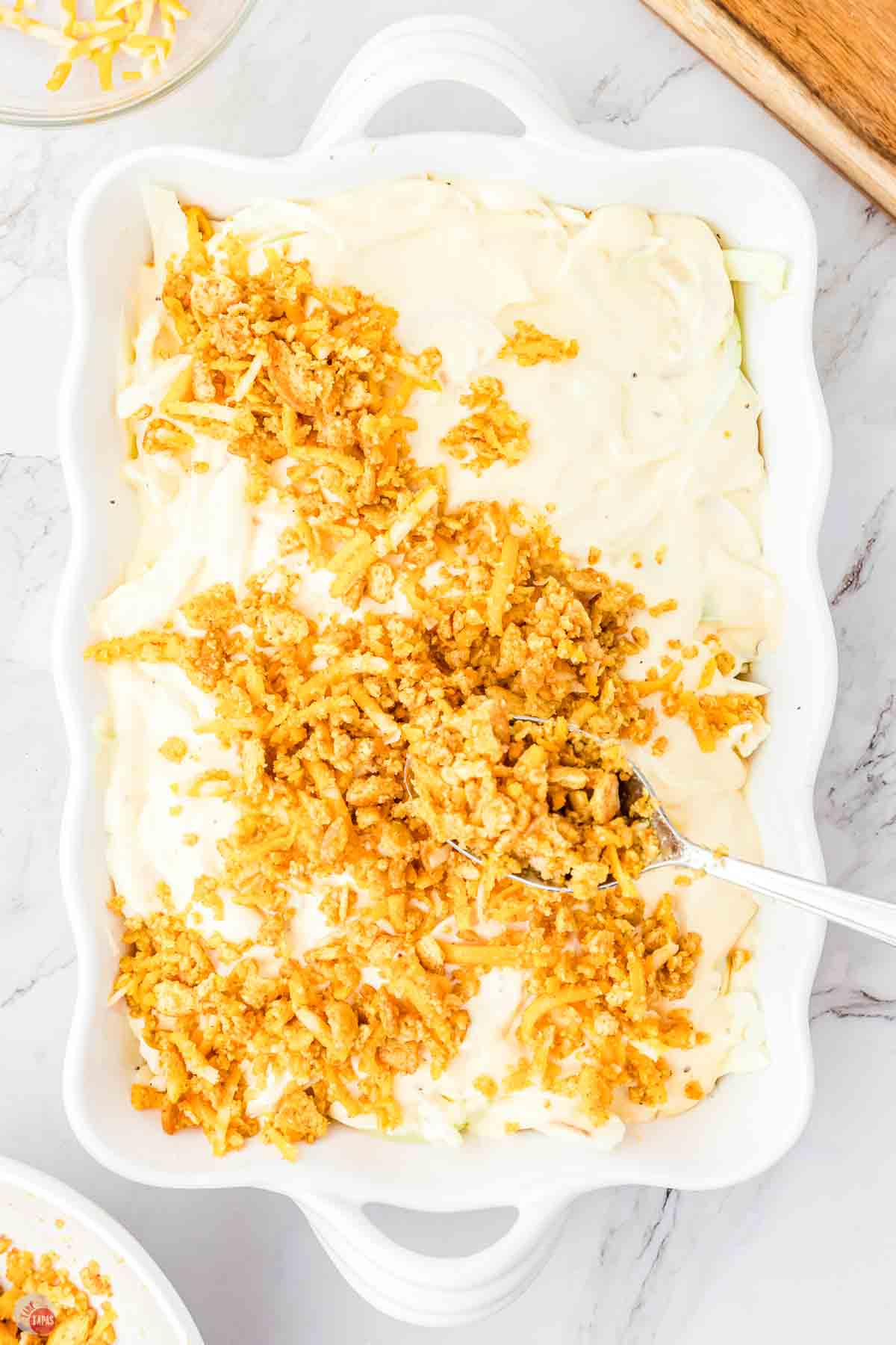 spoon sprinkling a crushed cracker topping over a casserole dish