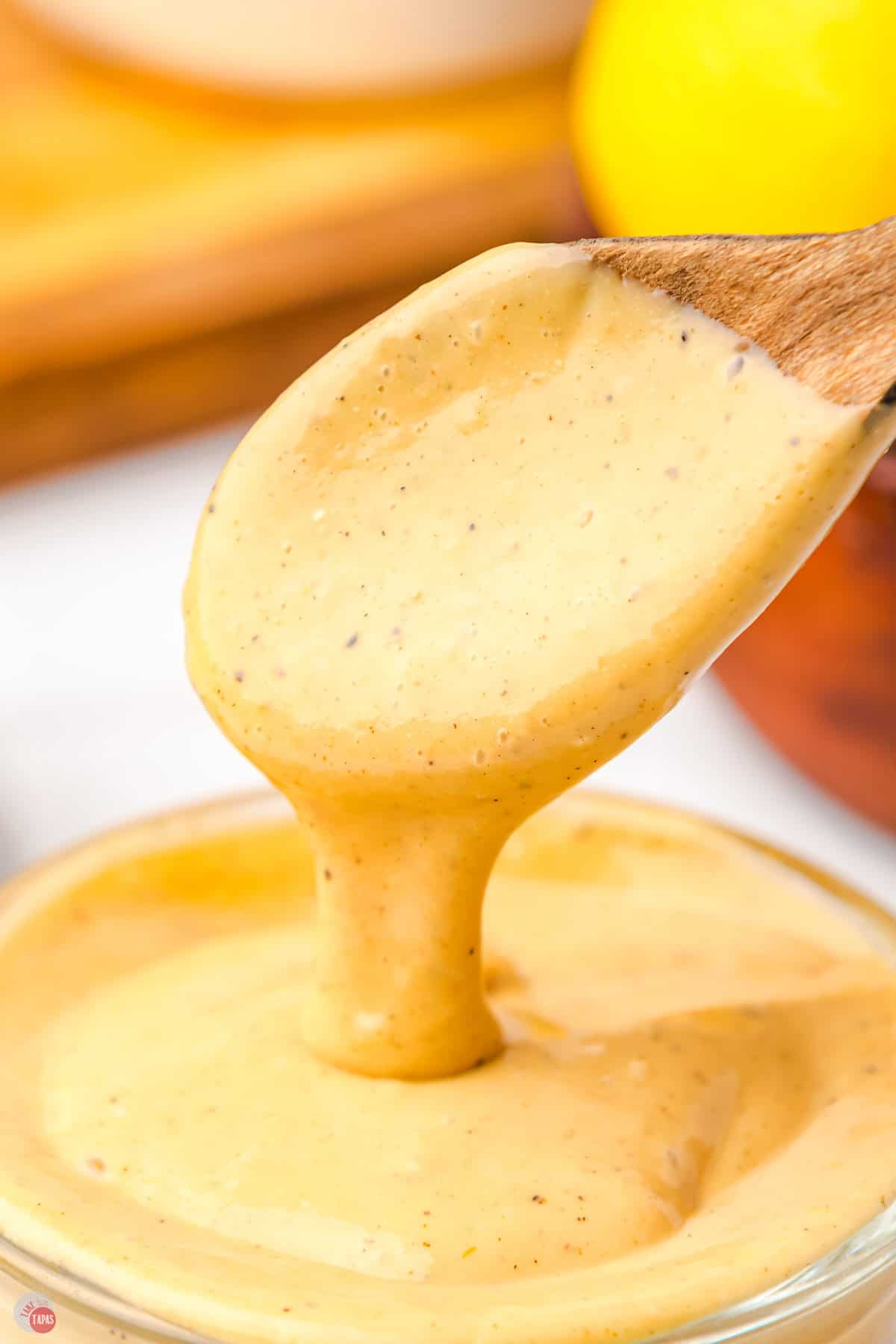 close up of a wood spoon pouring homemade caesar salad dressing into a dish