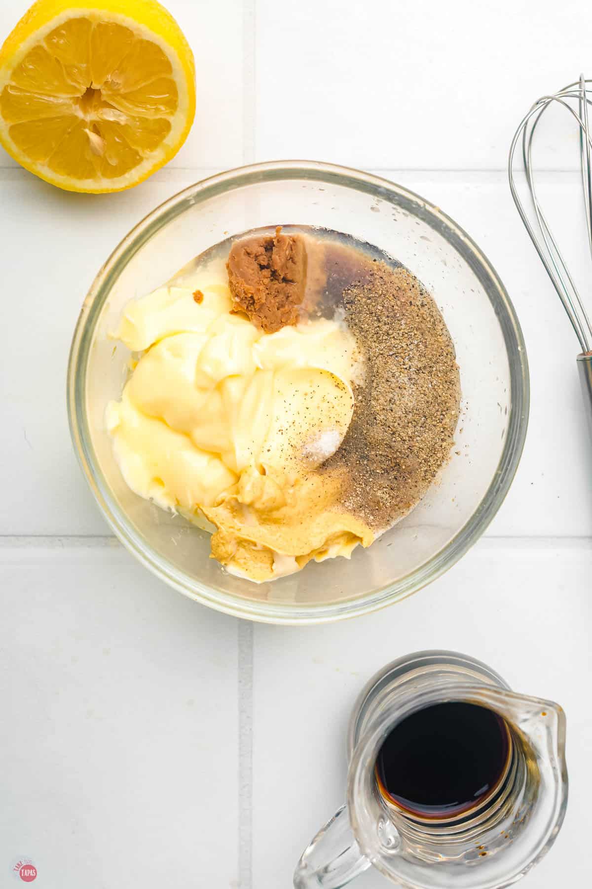 ingredients for a salad dressing in a clear bowl with a whisk next to it