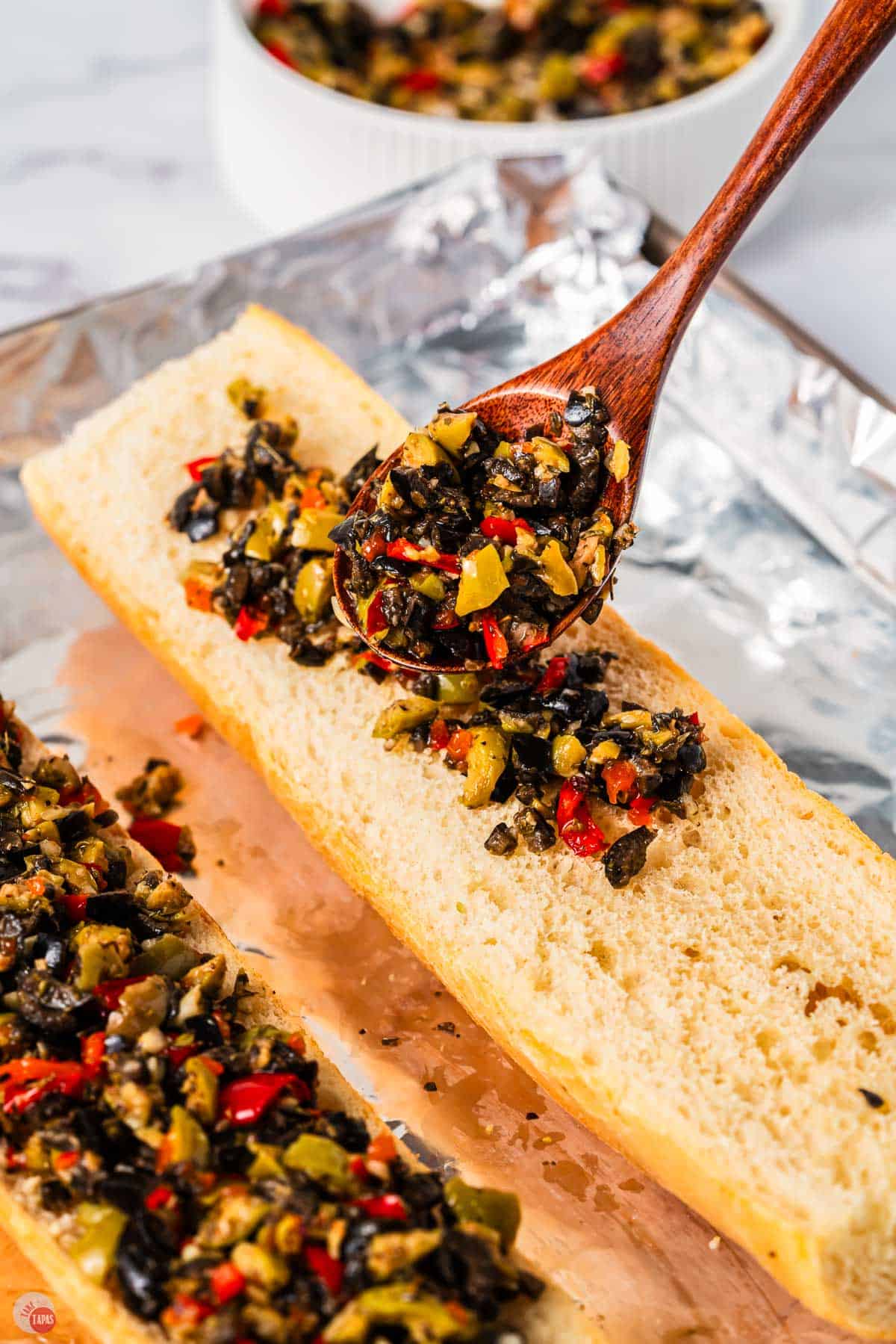 spoon pouring chopped olives on a piece of bread