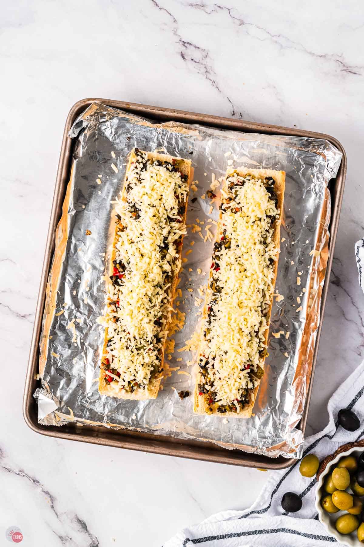 two pieces of french bread with cheese on a baking sheet with aluminum foil