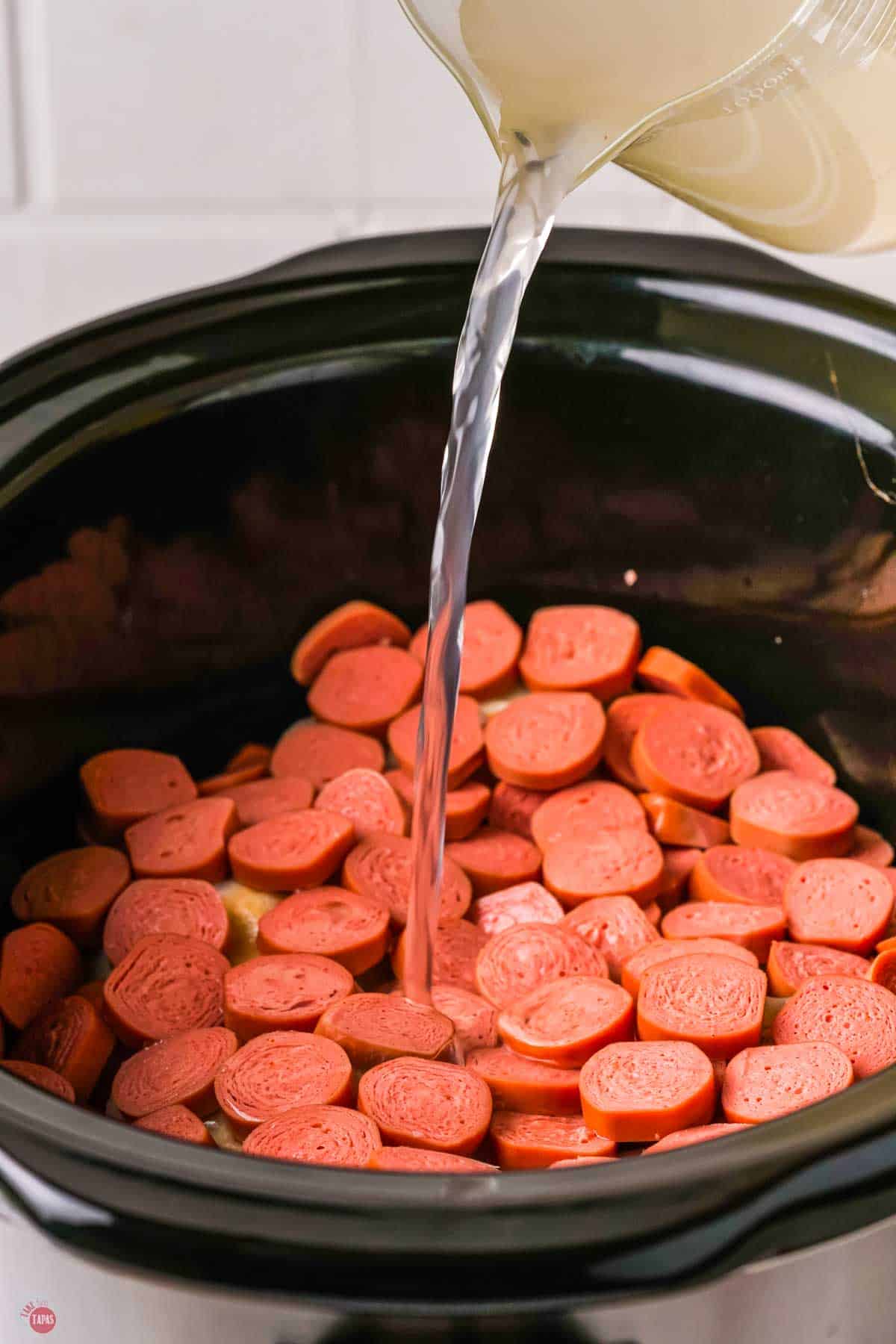 sliced kielbasa in a crockpot with water pouring in