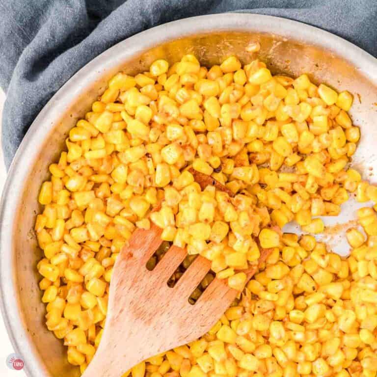 silver skillet with yellow corn and a wood spoon