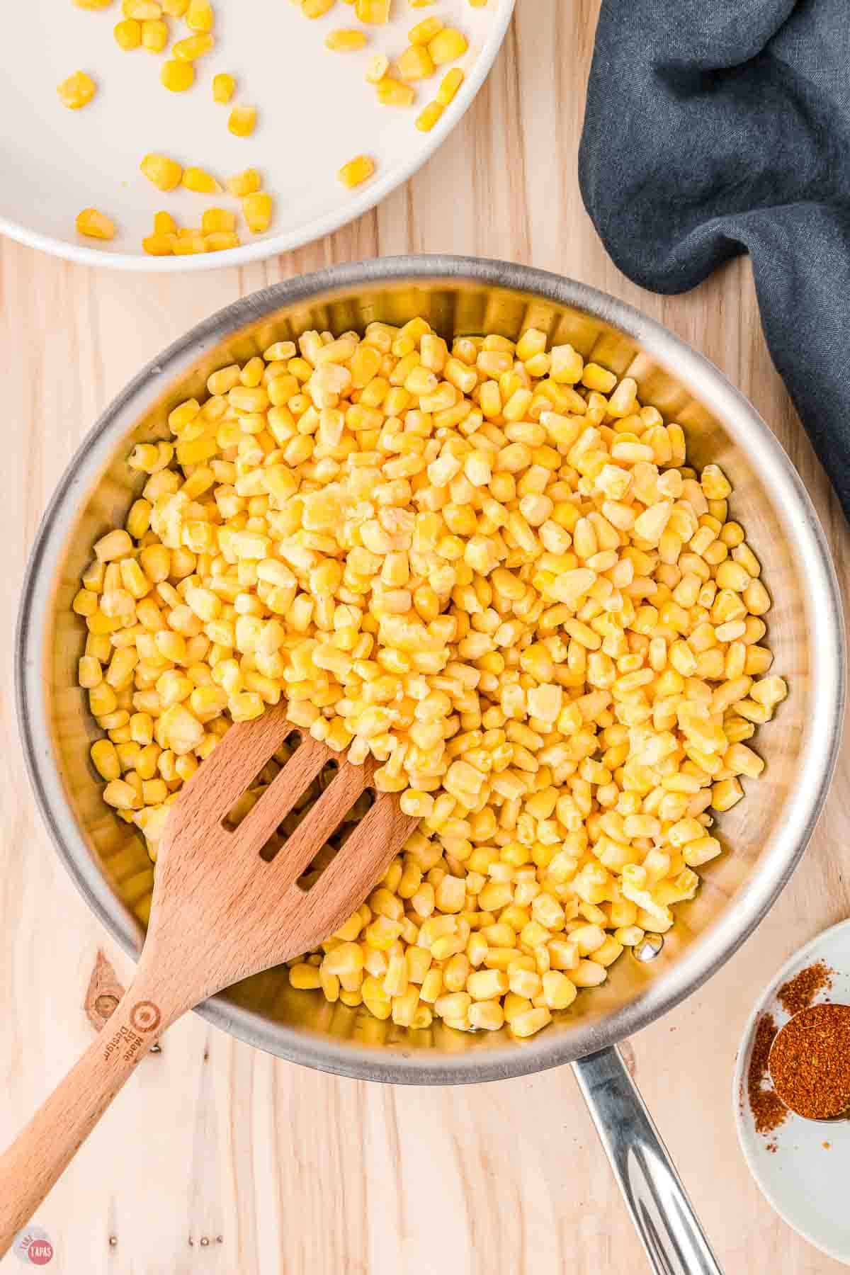 frozen corn kernels in a skillet with a slotted wood spatula
