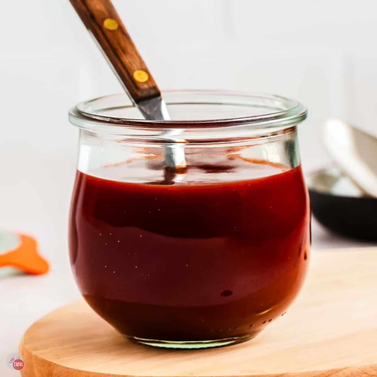 jar of bbq sauce on a wood board with a spoon
