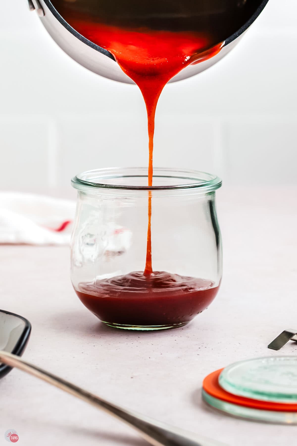 pot pouring red sauce into a clear jar