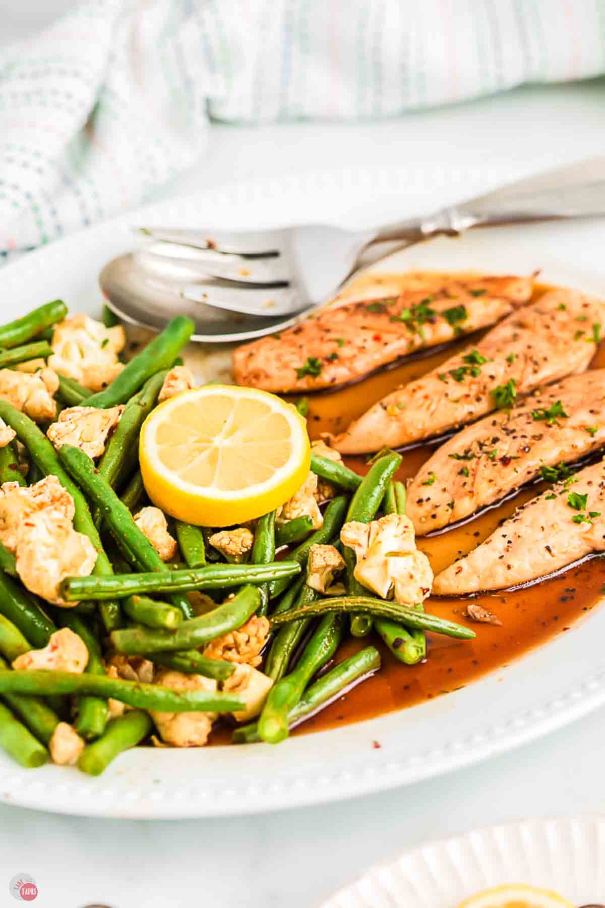 close up of green beans and meat on a platter with lemon slices and sauce
