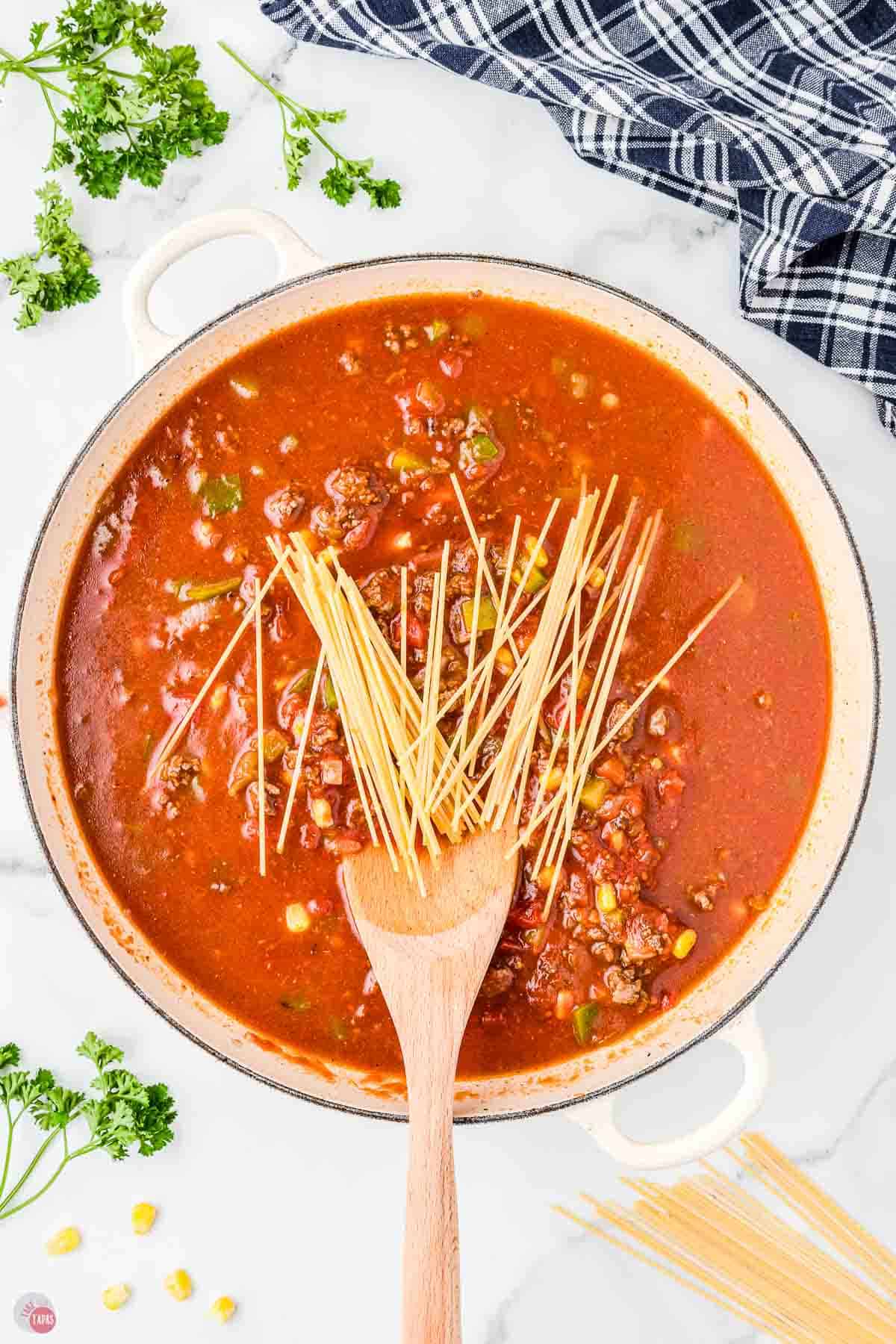 spaghetti sauce in a white pot with broken spaghetti noodles with a wood spoon