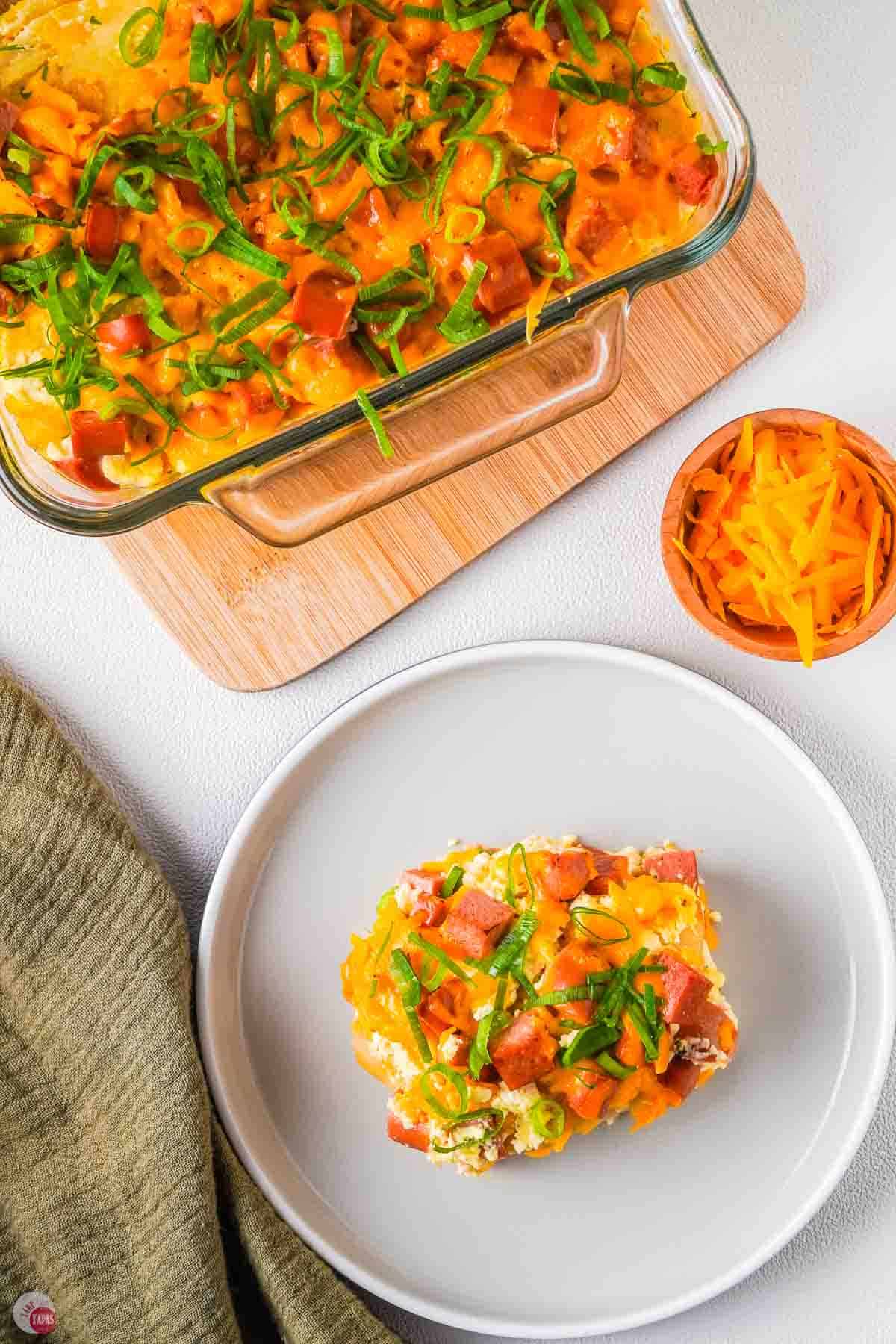 overhead picture of plate of food next to a clear baking dish on a wood cutting board