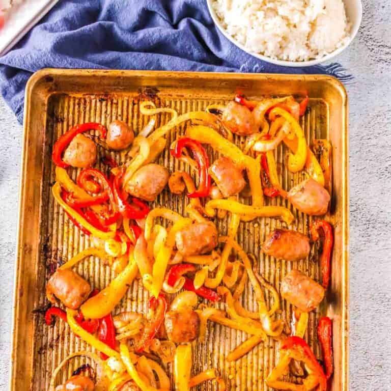 sheet pan with sausage and peppers on it with a blue napkin next to it