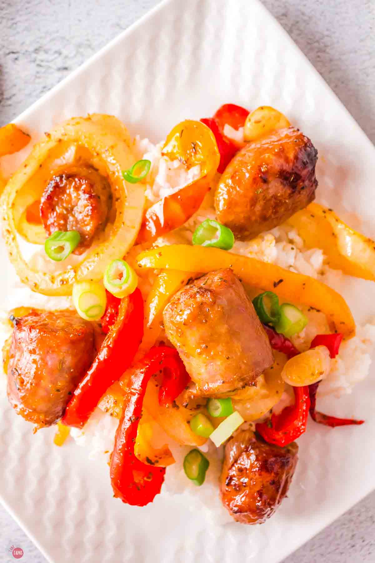 sausage peppers and onions on rice and a white plate