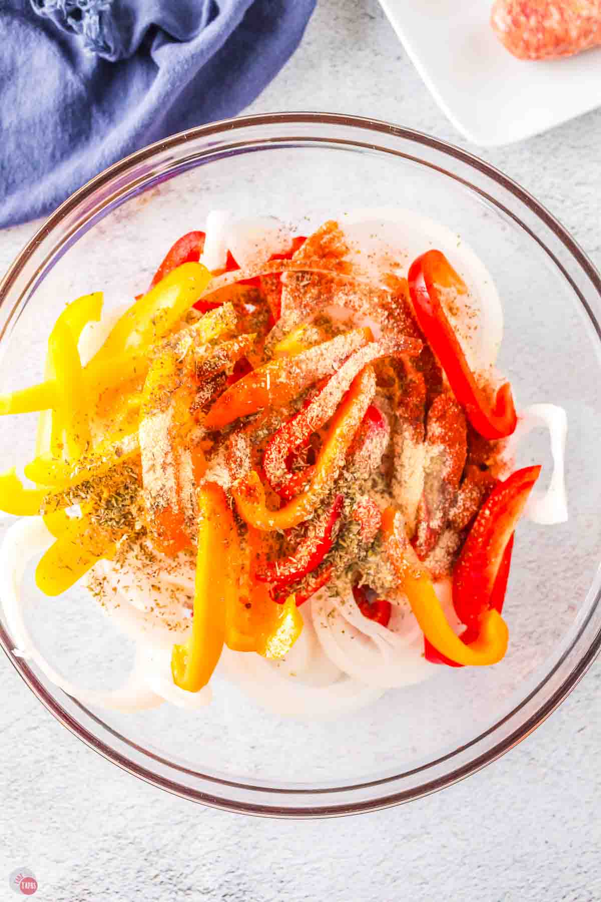 clear bowl with sliced bell peppers and onions topped with spices
