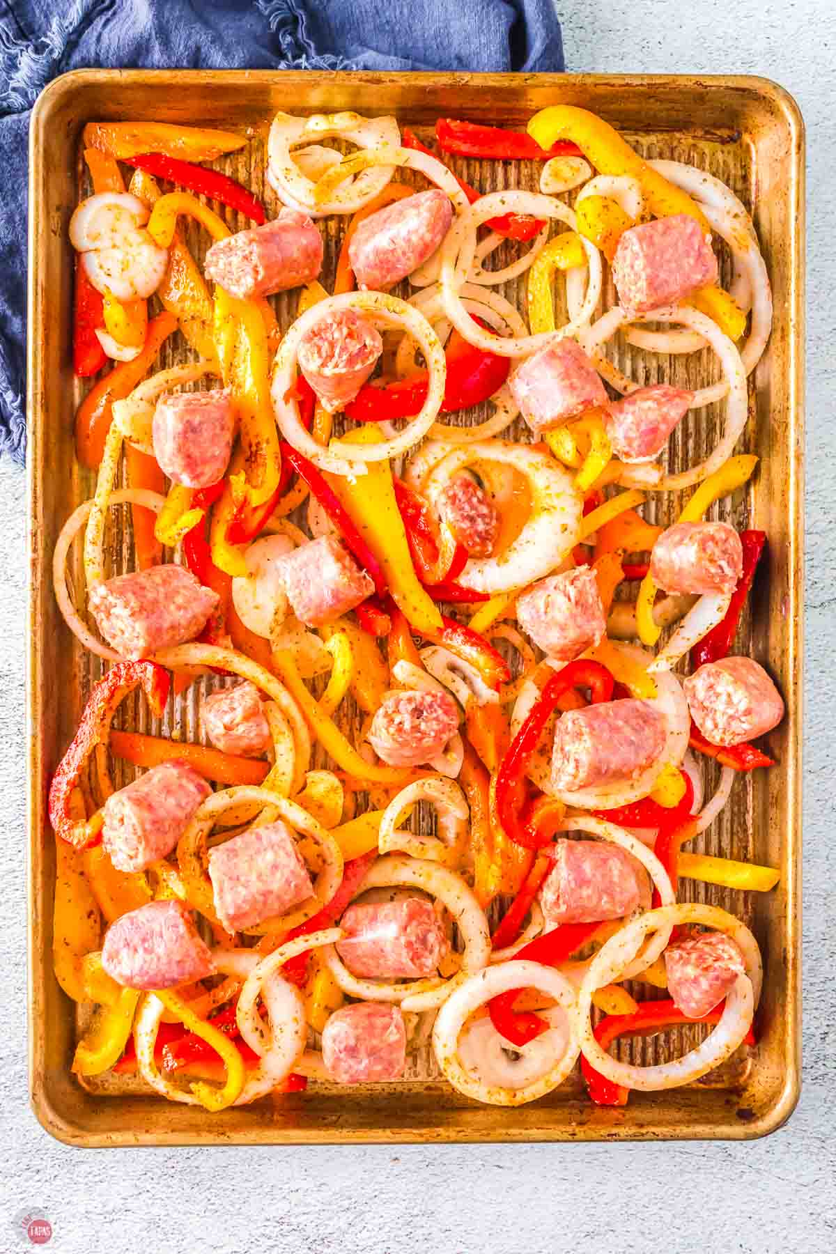 onions, peppers, and pieces of sausage on a sheet pan