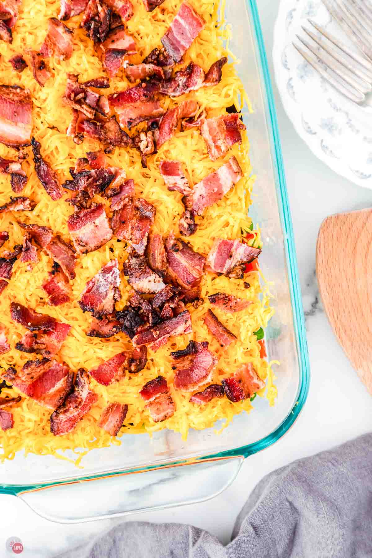 close up of cheese and bacon in a clear dish with a wood spoon