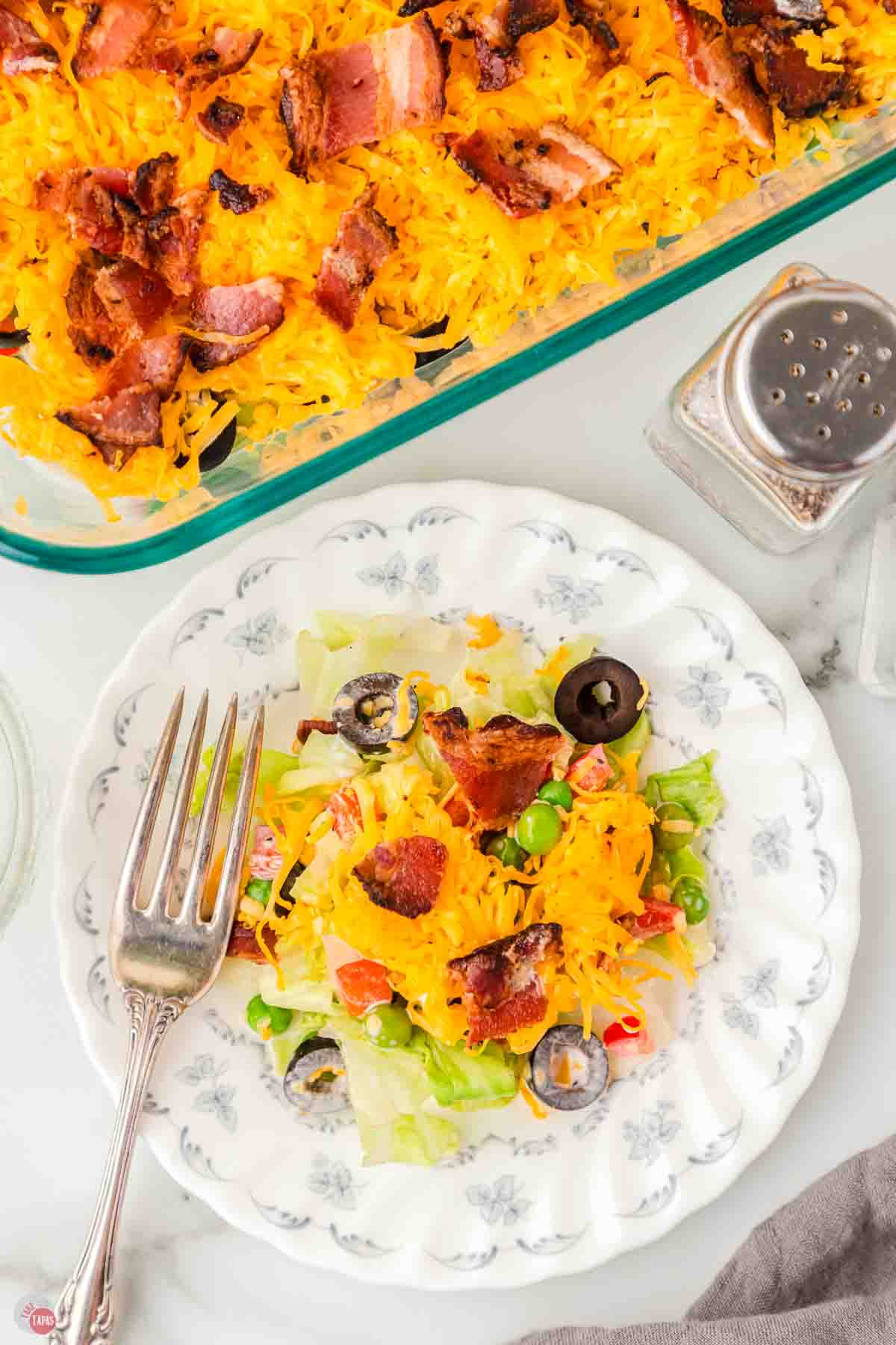 overhead picture of plate with lettuce and cheese next to a casserole dish and salt and pepper shakers.