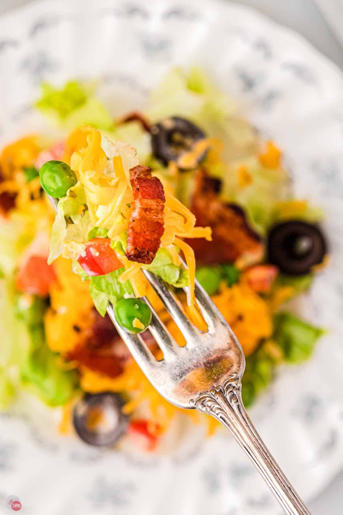 close up of fork with lettuce, cheese, and bacon on it