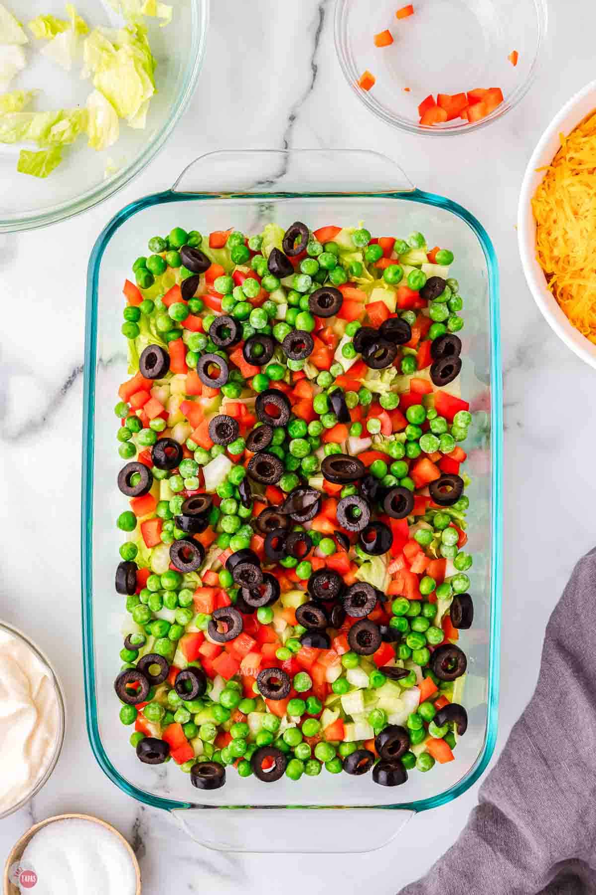casserole dish with tomatoes, olives, and peas in it