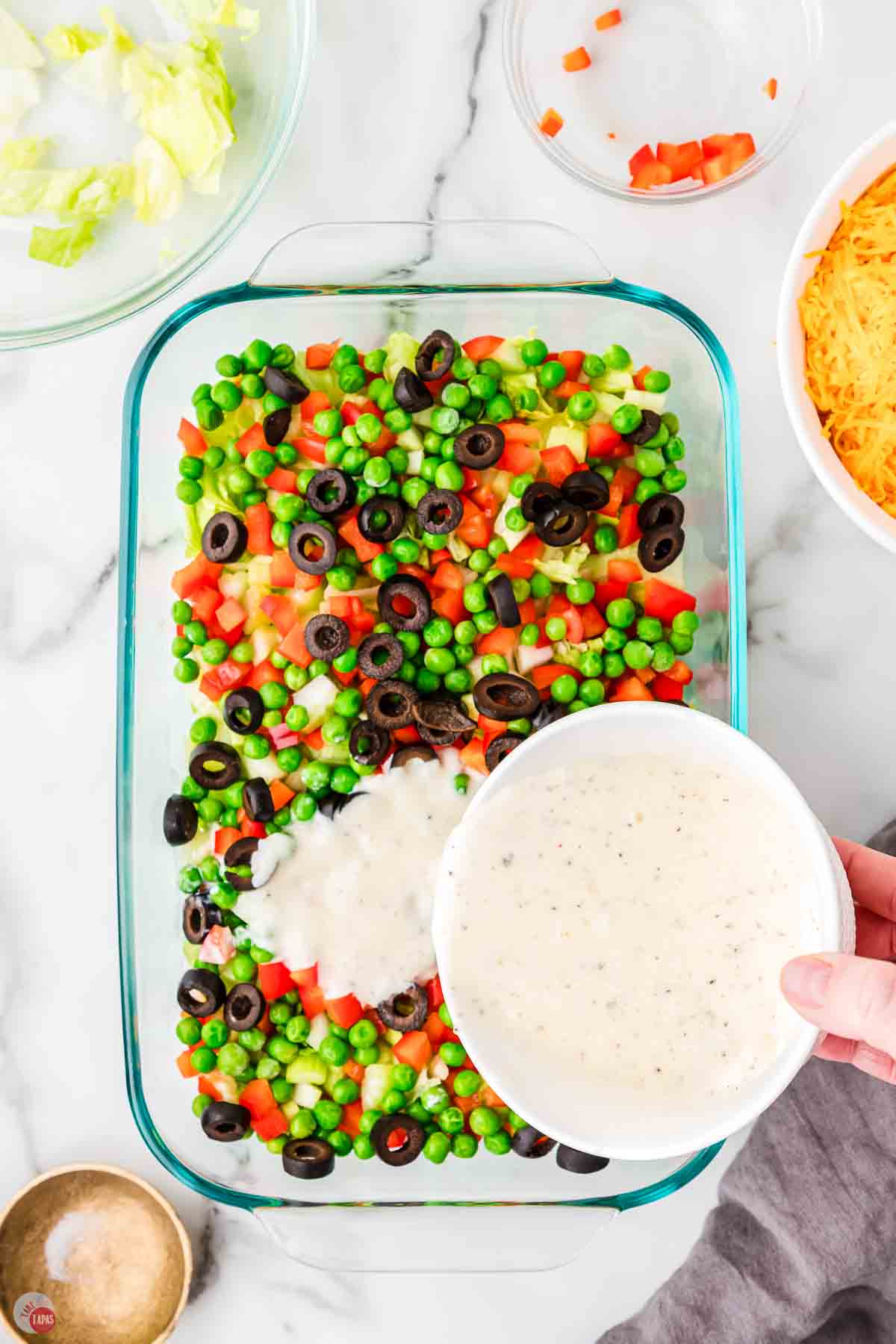 bowl of dressing being poured on top of peas and olives