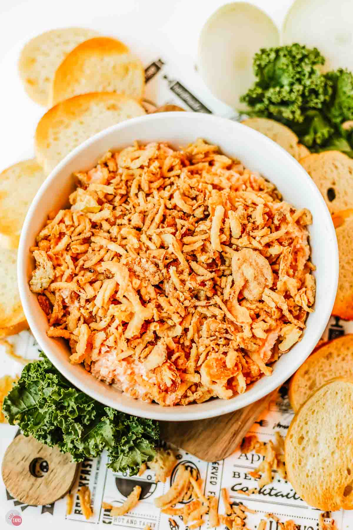 white bowl with fried onions in it, surrounded by parsley clusters