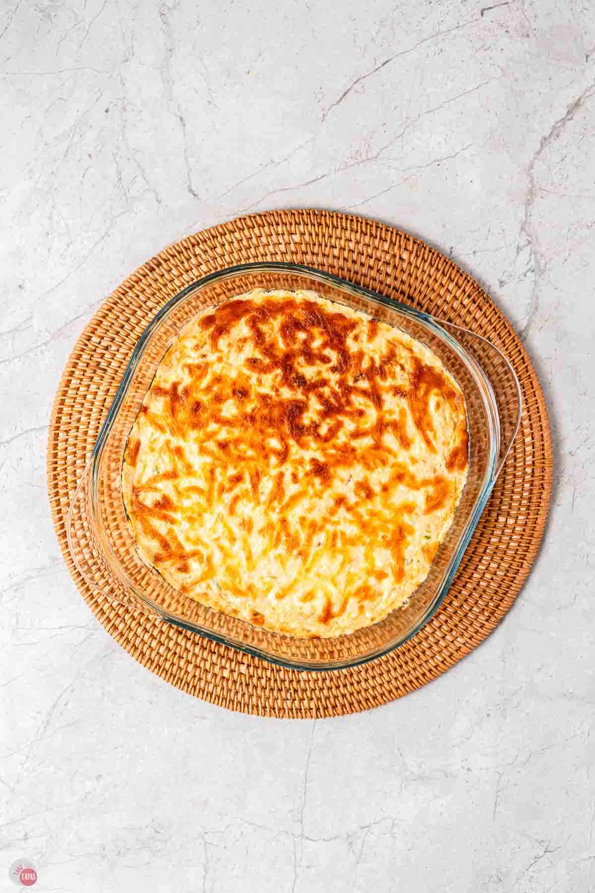 baked cheesy dip in a clear bowl on a wood circle platter