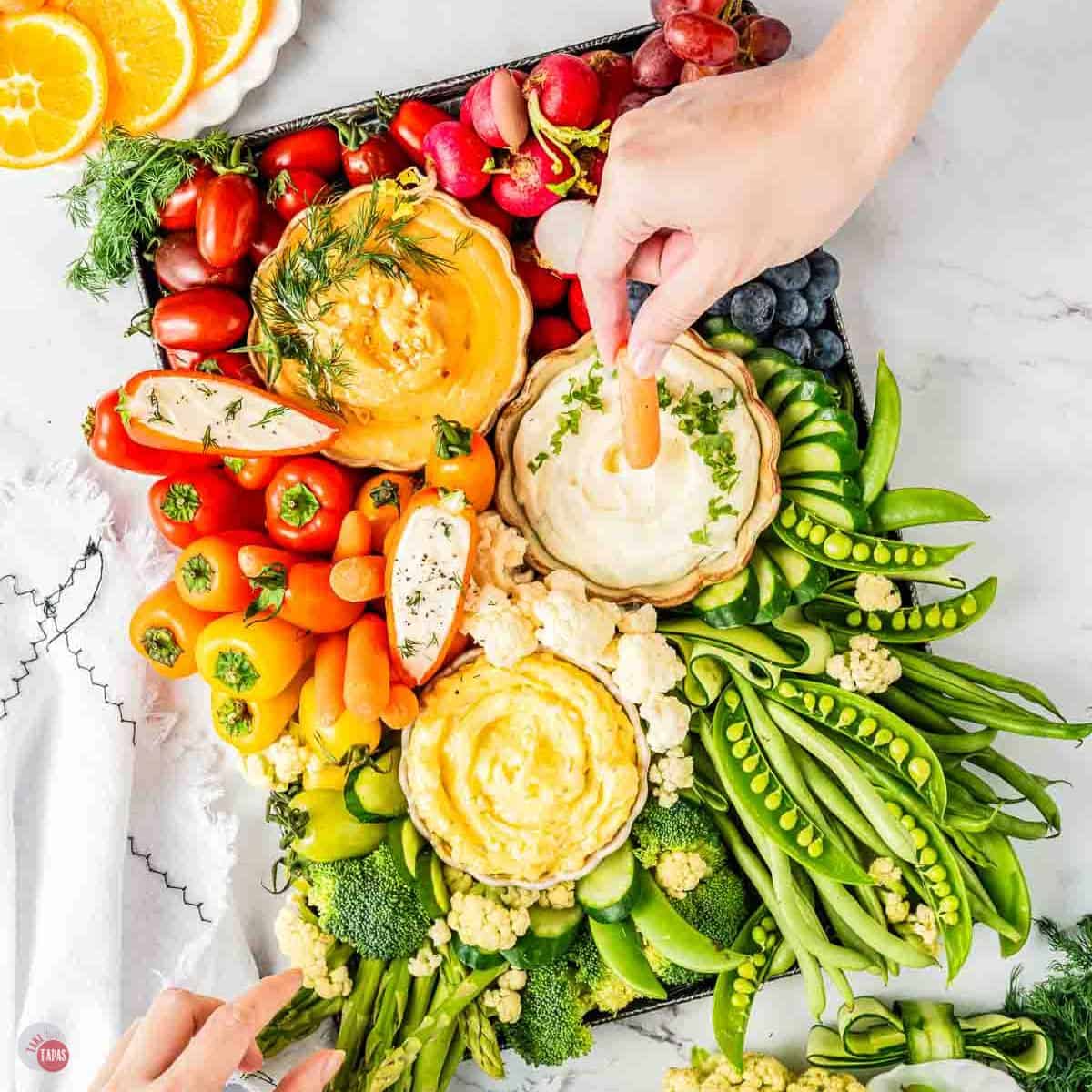 Colorful vegetable platter featuring cherry tomatoes, bell peppers, cucumbers, and dips.