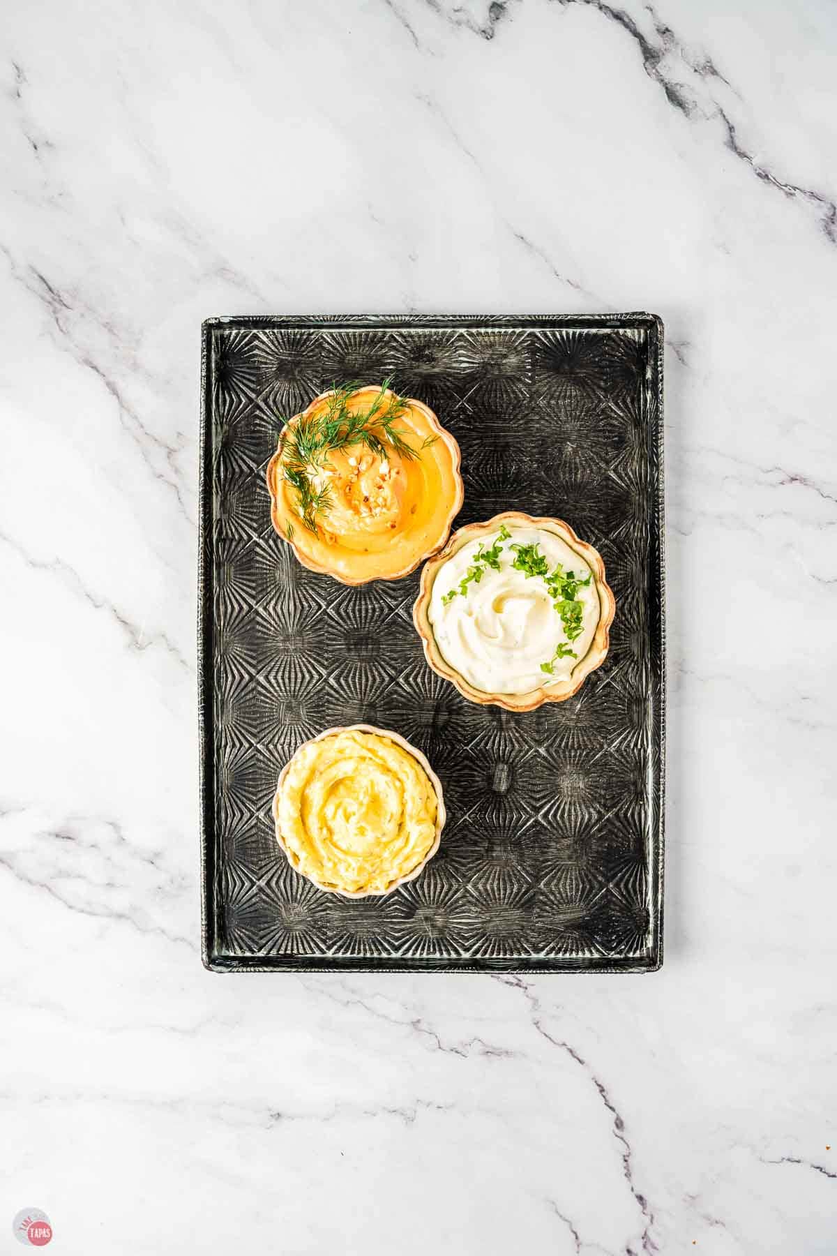 Assorted dips in bowls on a black textured serving tray.