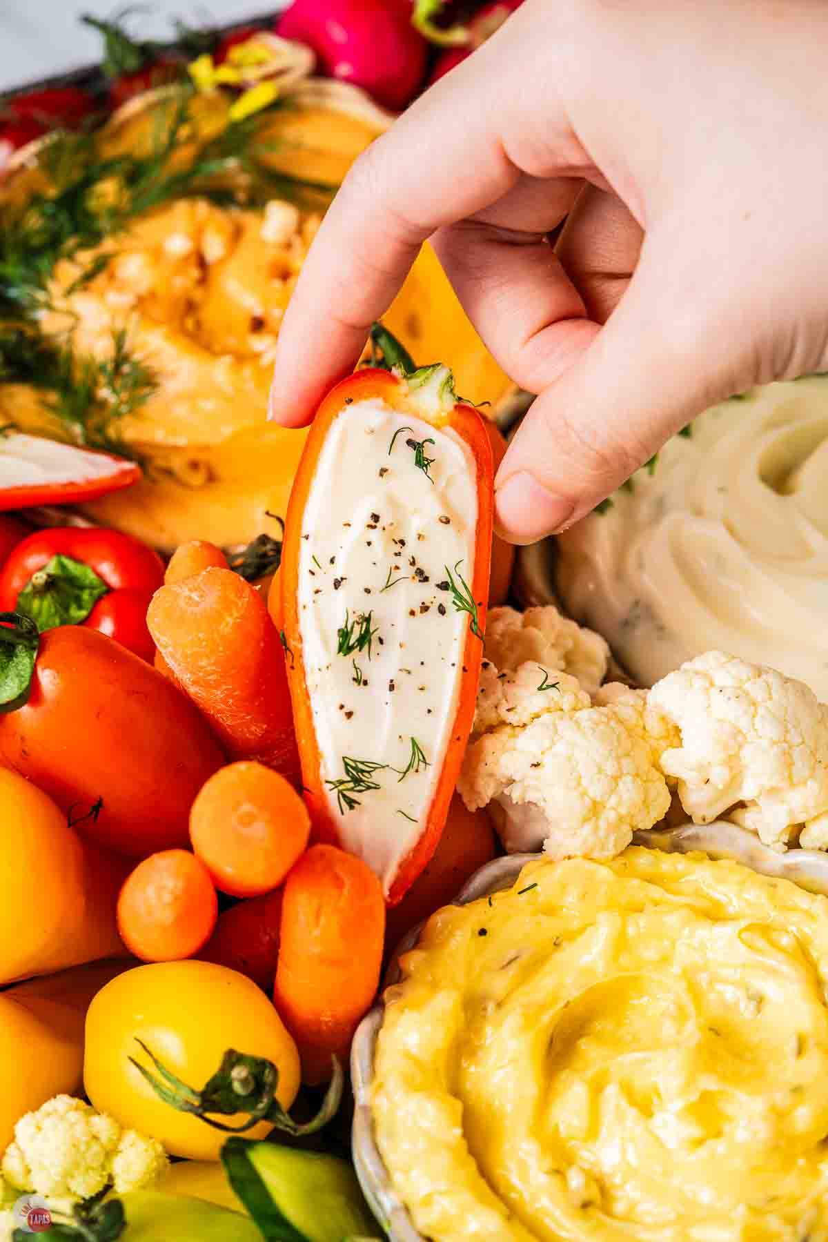 hand holding a stuffed mini bell peppers surrounded by vegetables