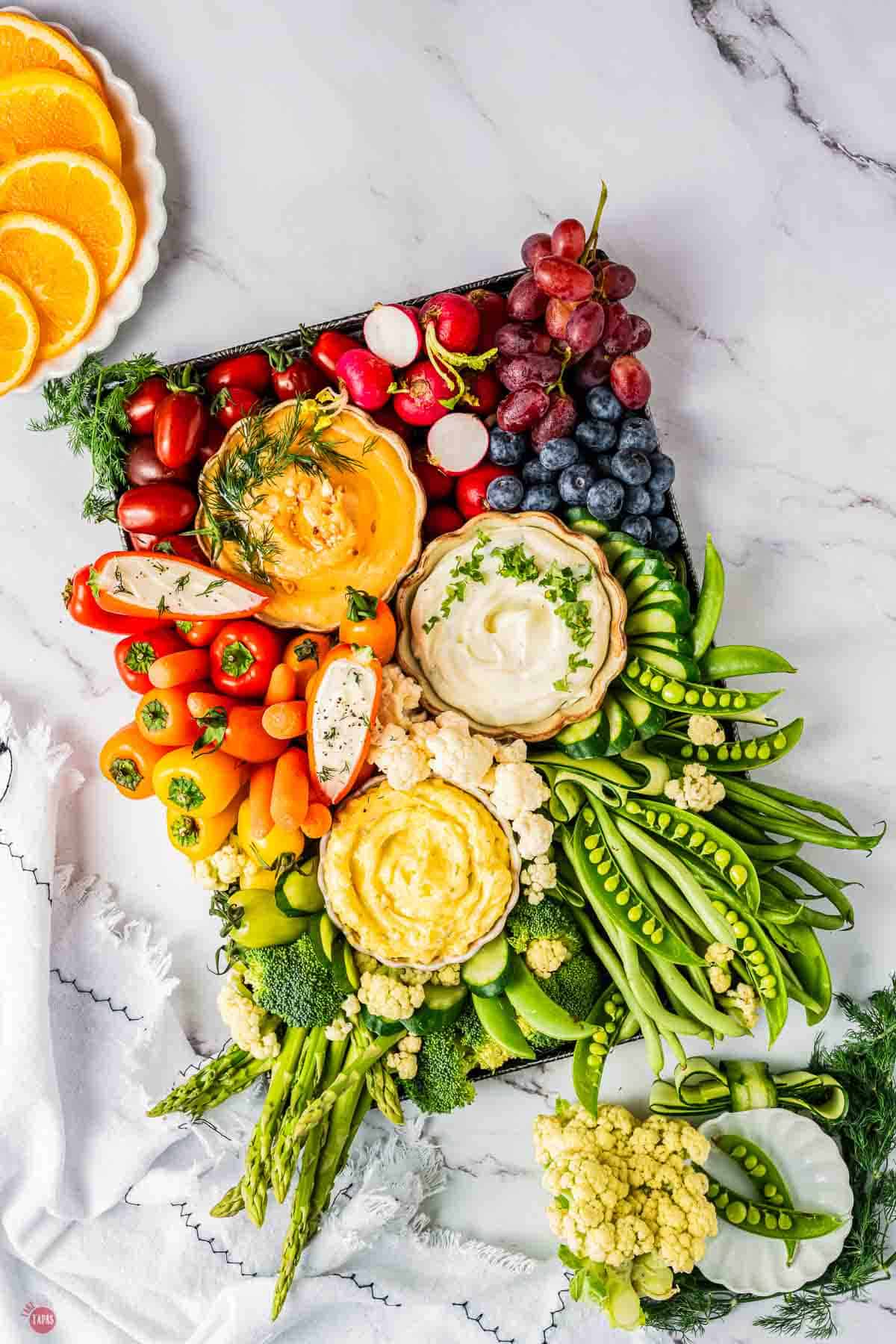 Colorful vegetable and fruit platter with cherry tomatoes, grapes, radishes, and sliced cucumbers.