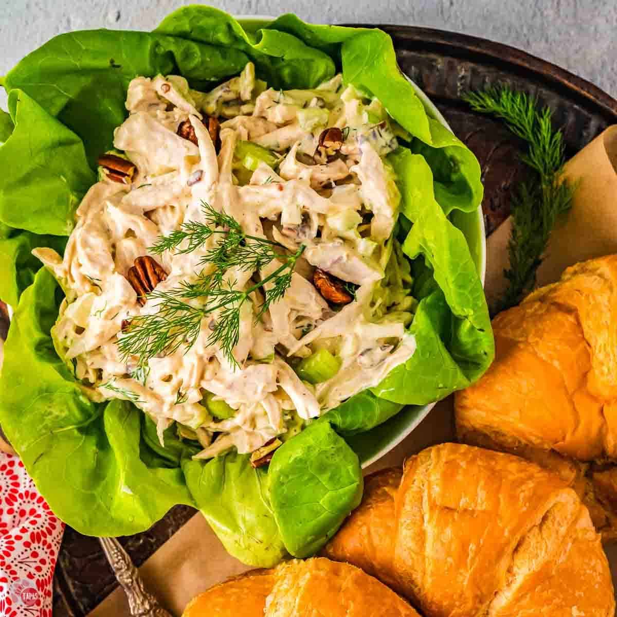 lettuce bowl filled with chicken salad surrounded by croissants