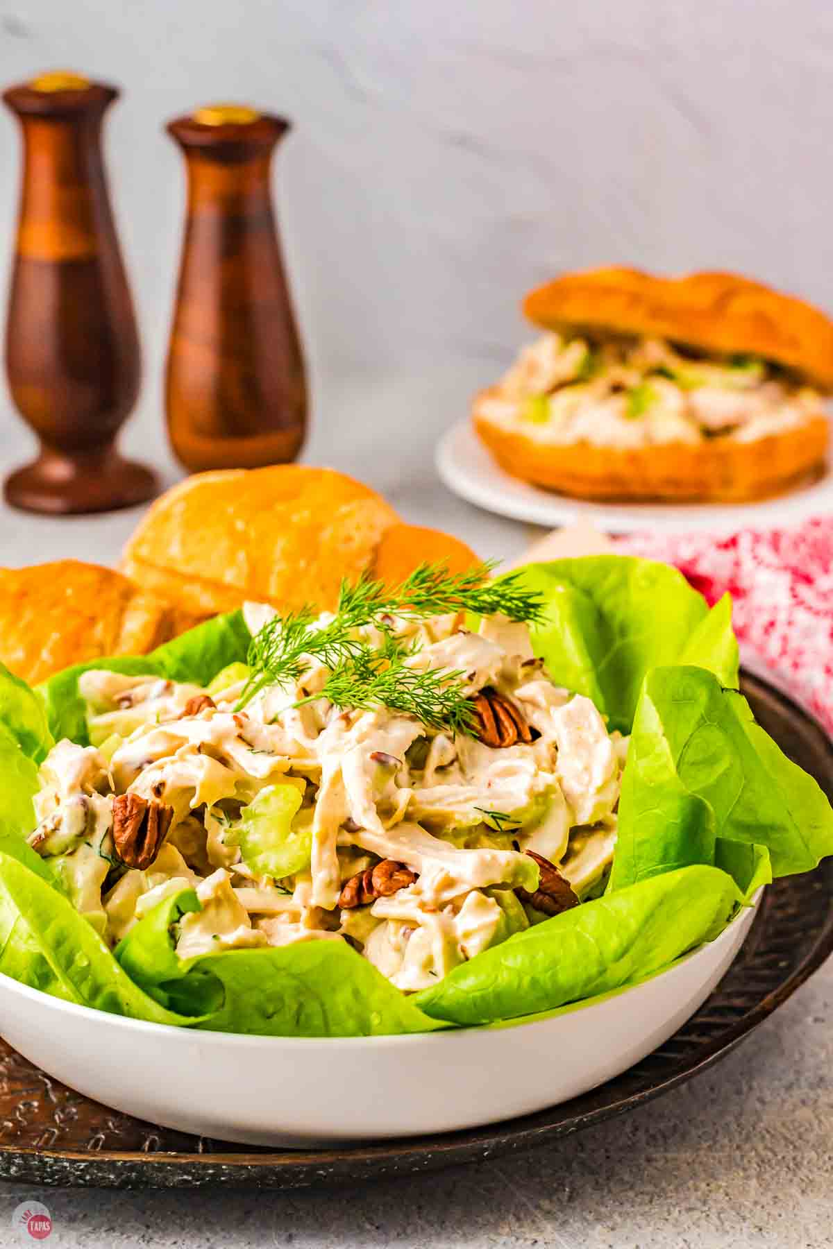 white bowl with large lettuce leaf and a scoop of chicken salad and a sandwich in the background