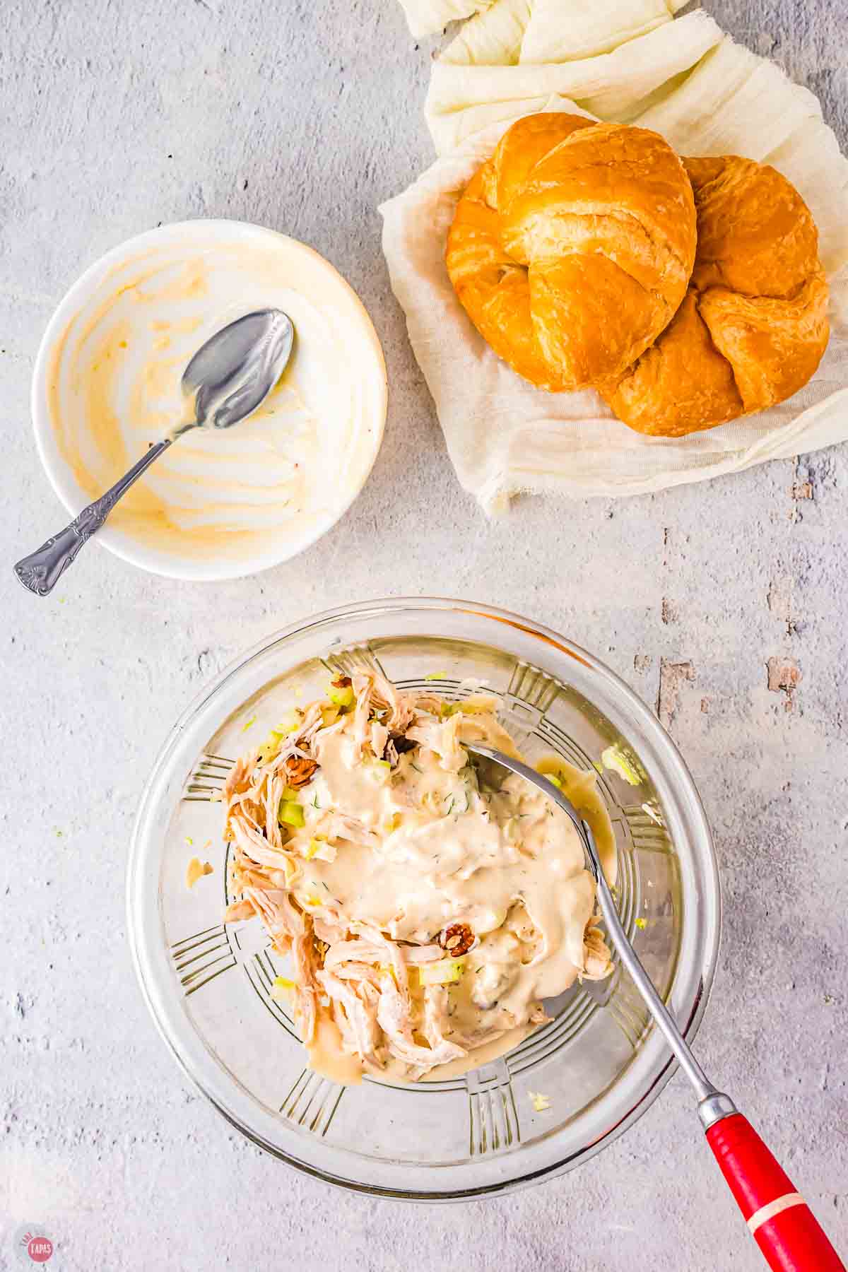 clear bowl with chopped chicken and a mayo dressing in it with a plate holding 2 croissants