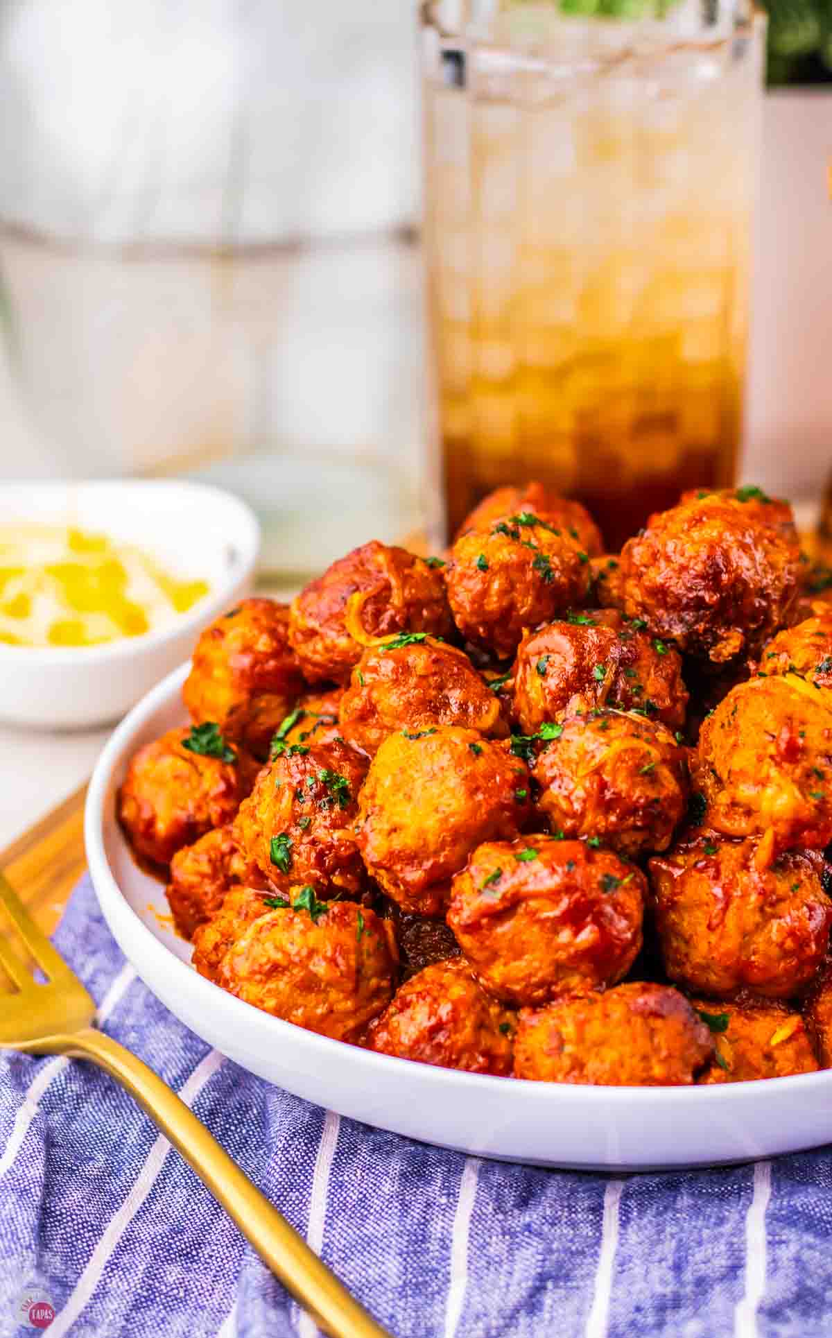 close up of meatballs on a white plate with a drink behind it
