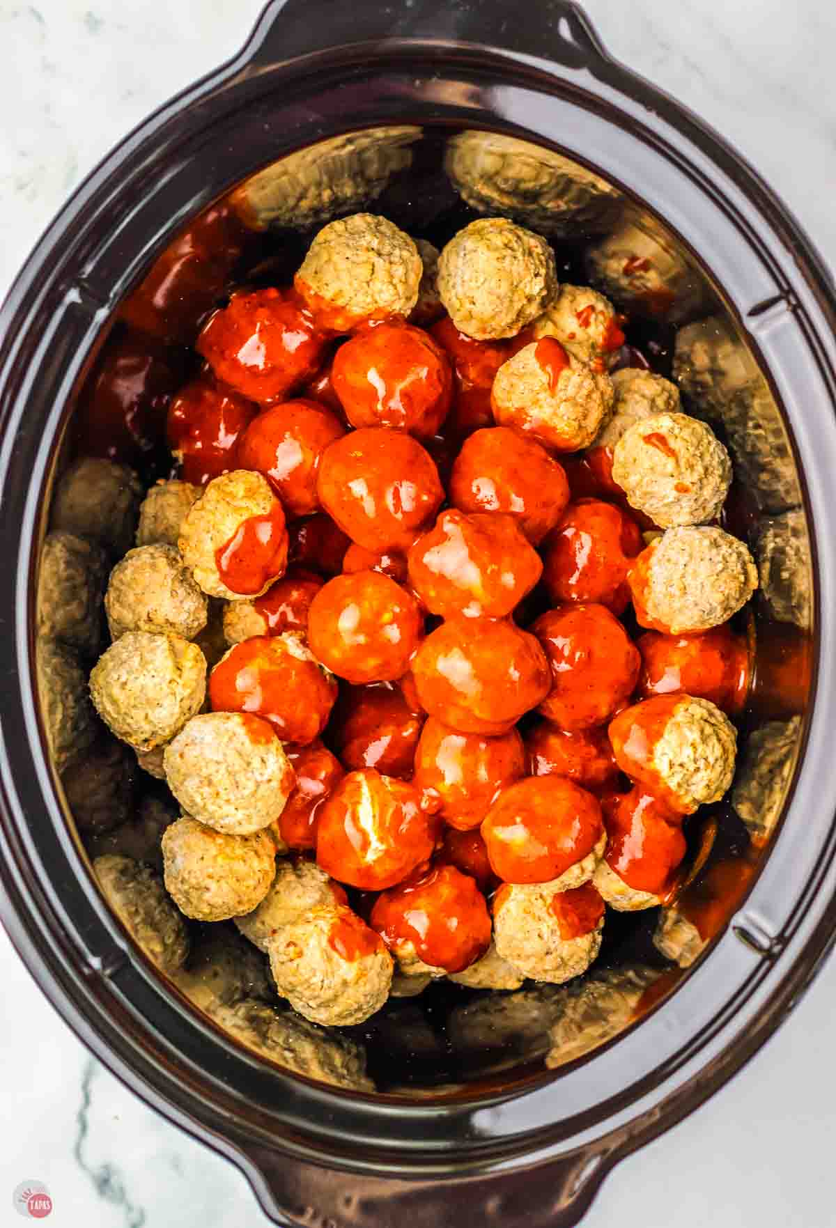 black slow cooker with frozen meatballs and sauce in it