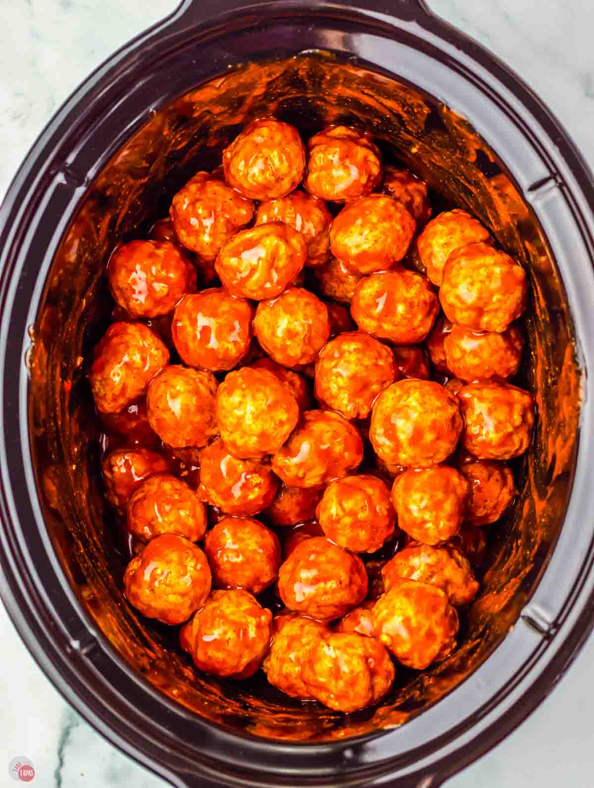 crockpot with meatballs and enchilada sauce on them