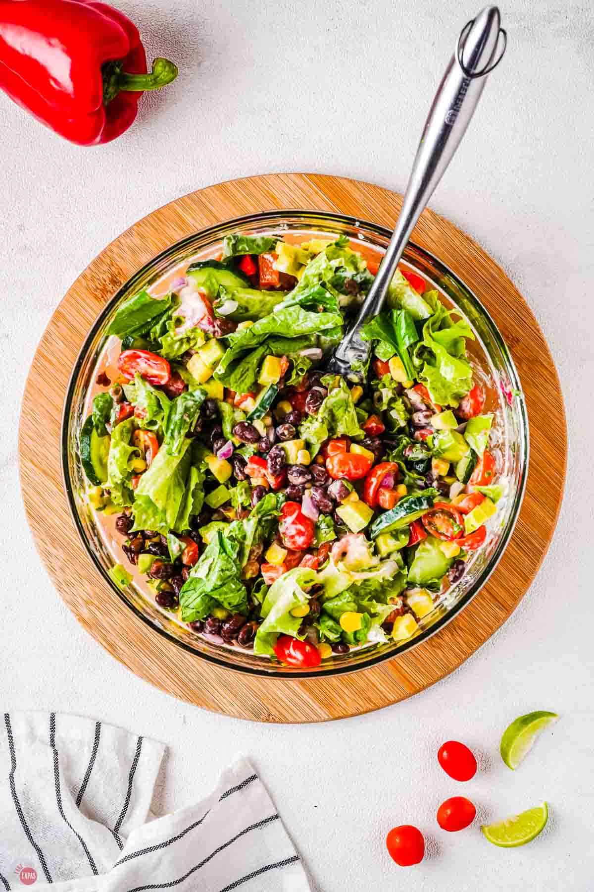 wood circle with clear bowl full of salad and a silver spoon